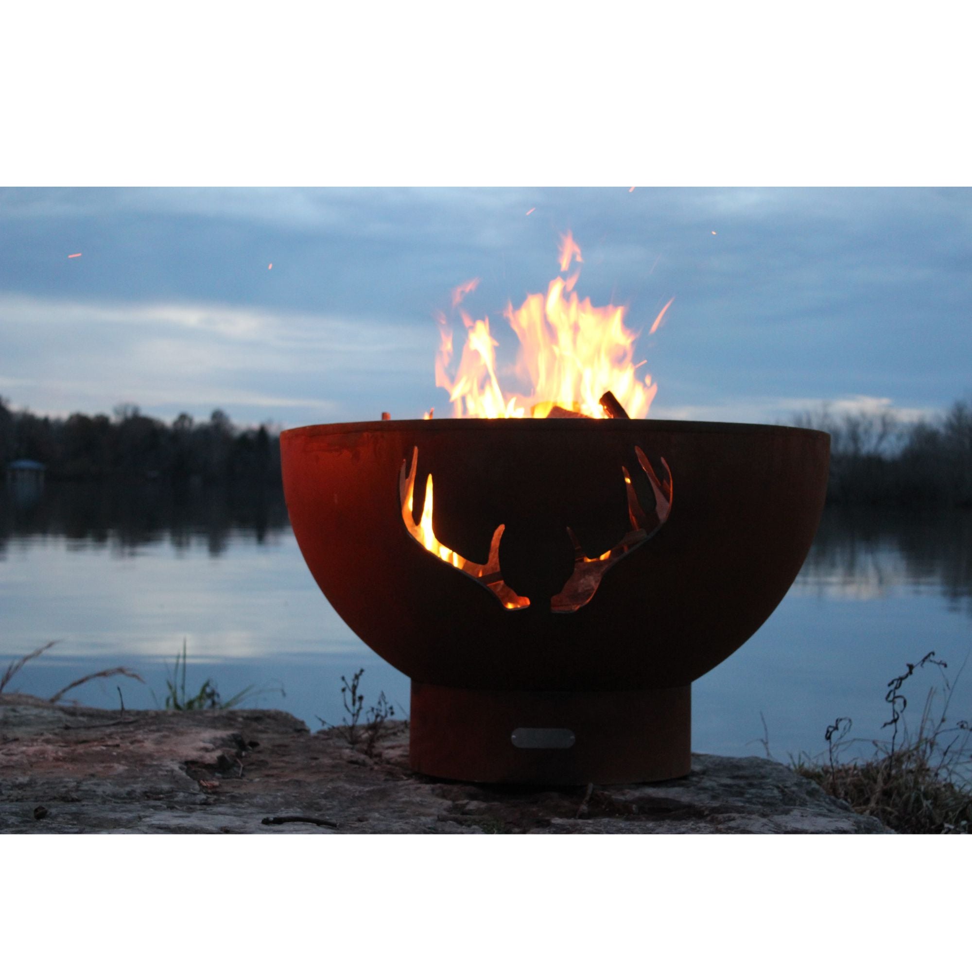 Fire pit with flames burning near a body of water at dusk
