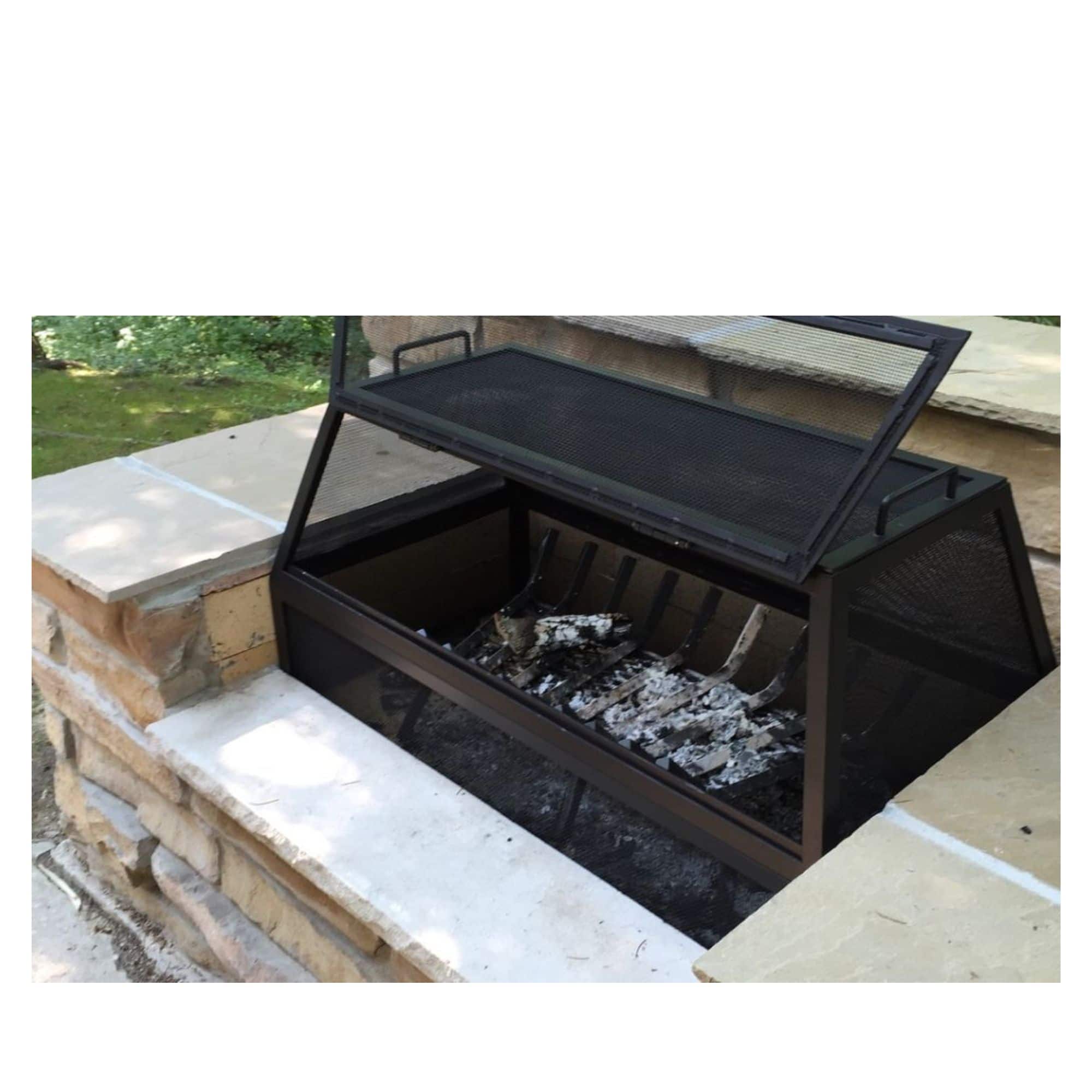 A black metal outdoor fire pit with a mesh screen lid, shown open with ash and embers inside, set into a stone patio structure outdoors.