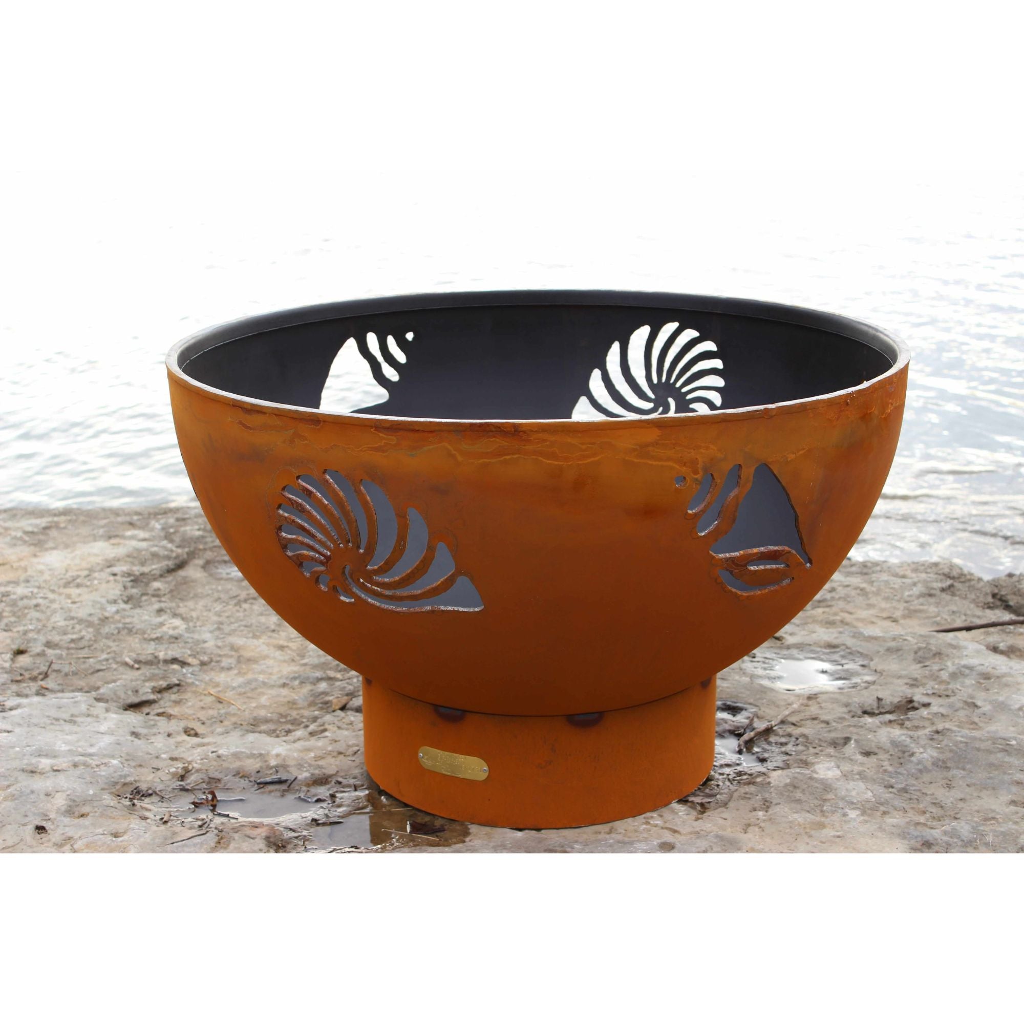 Rust-colored fire pit with cut-out designs on a stone surface