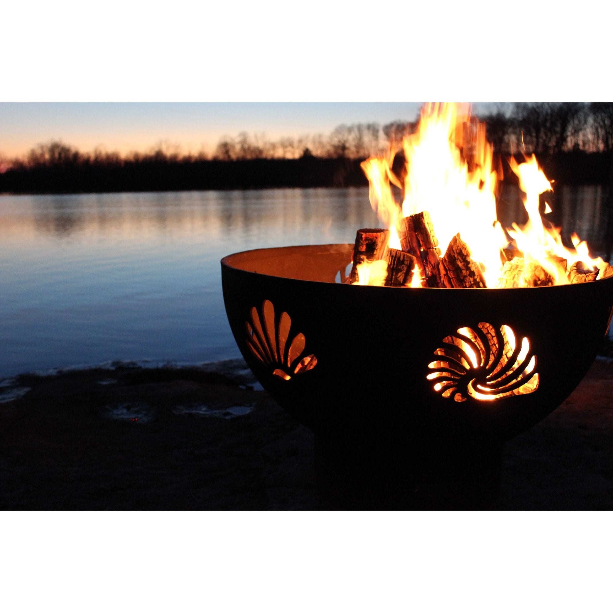 Fire pit with flames burning near a body of water at sunset