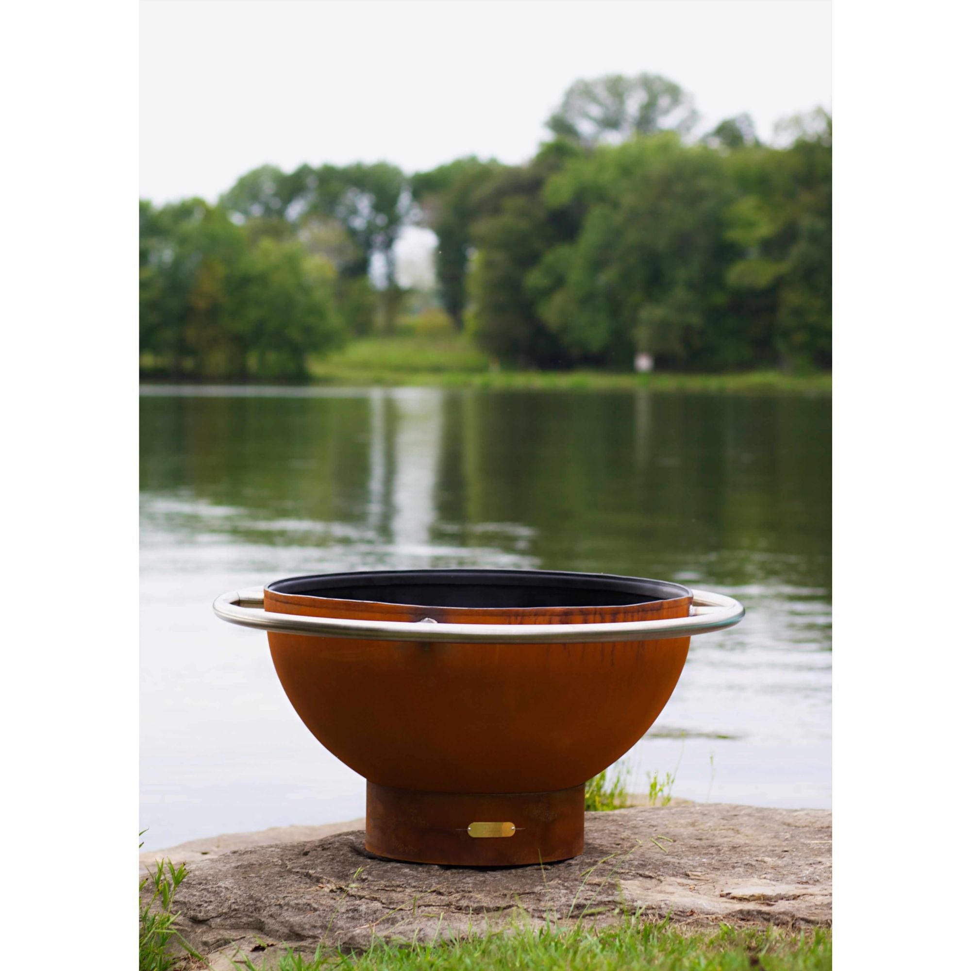 Bronze fire pit with black interior on a stone ledge by a lake