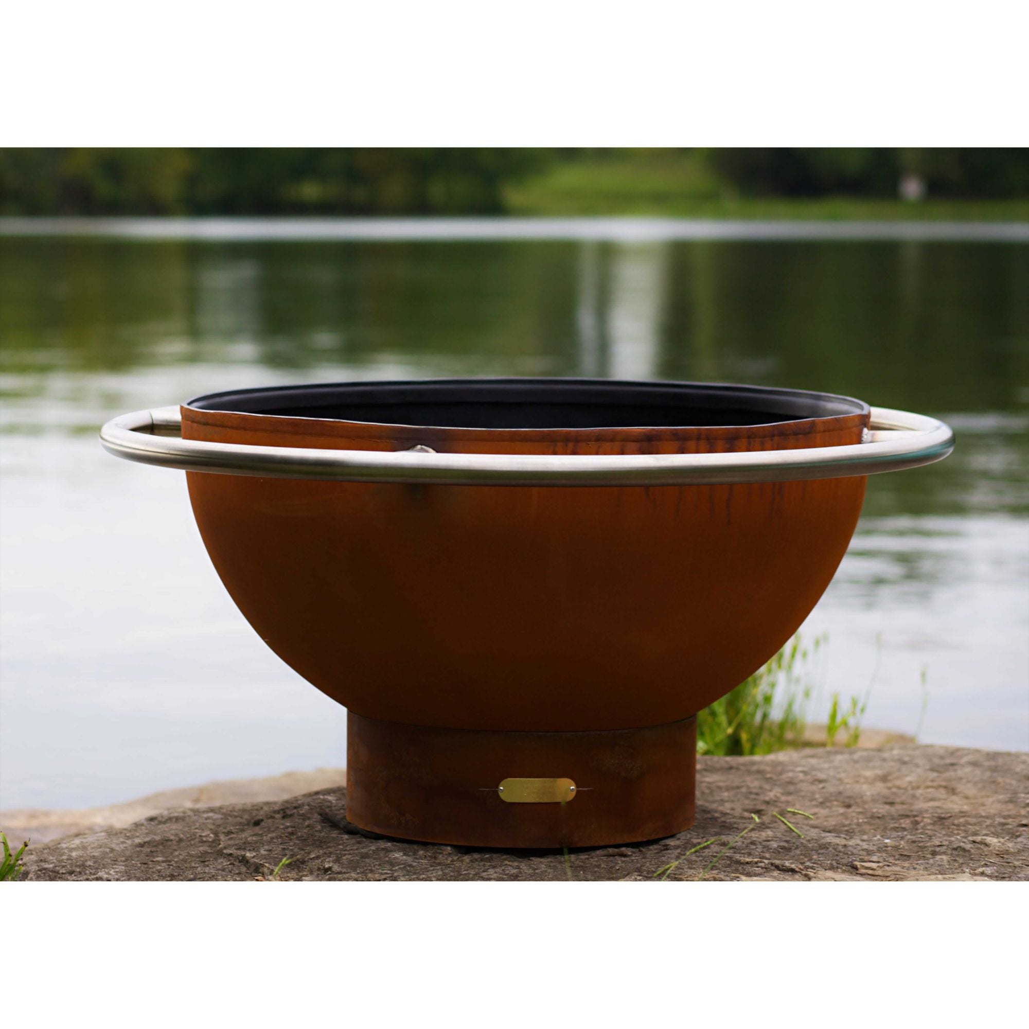 Rust-colored fire pit with a black interior on a lakeside setting