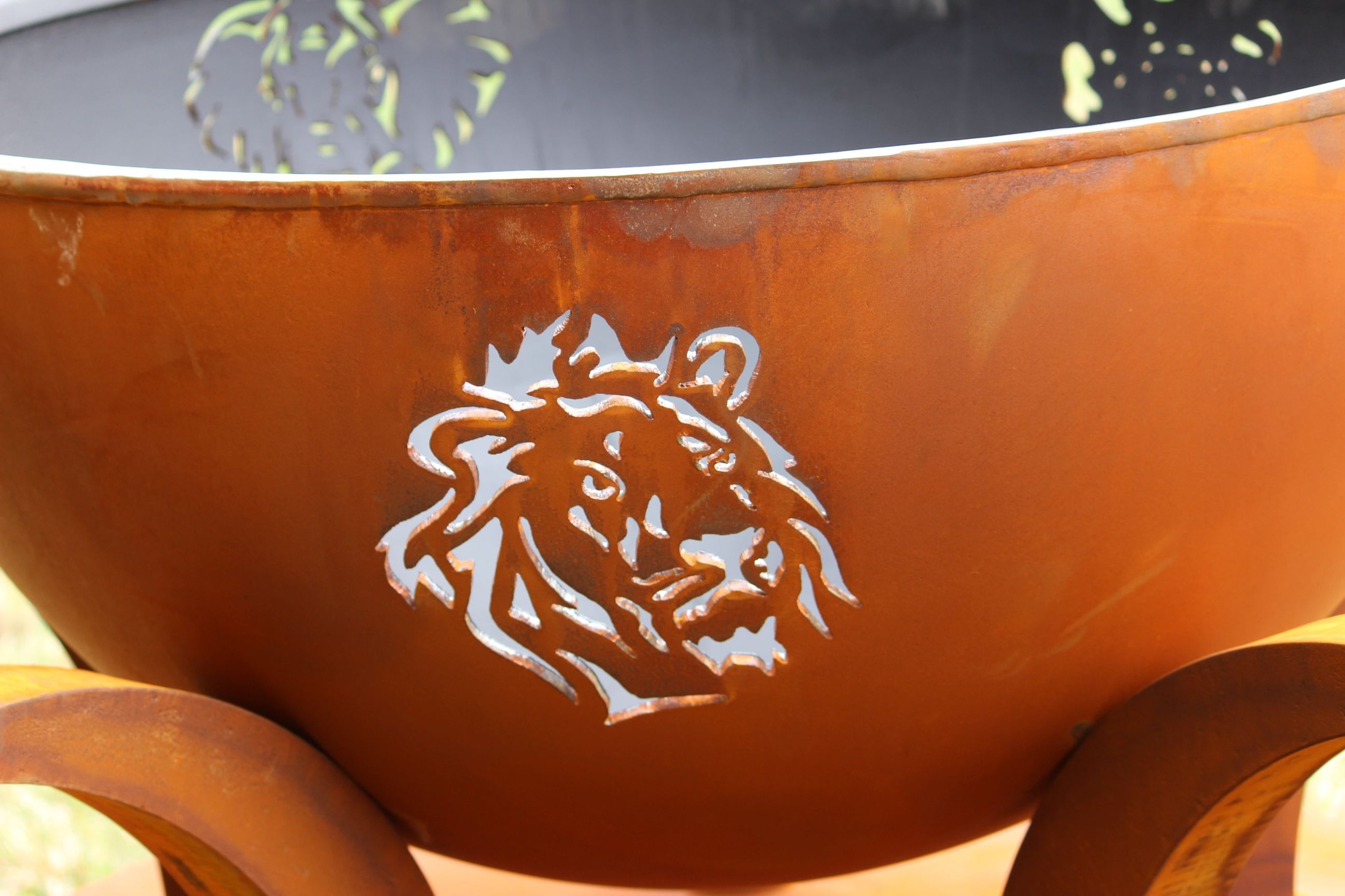 Rust-colored metal fire pit with a lion's head design on a blurred background