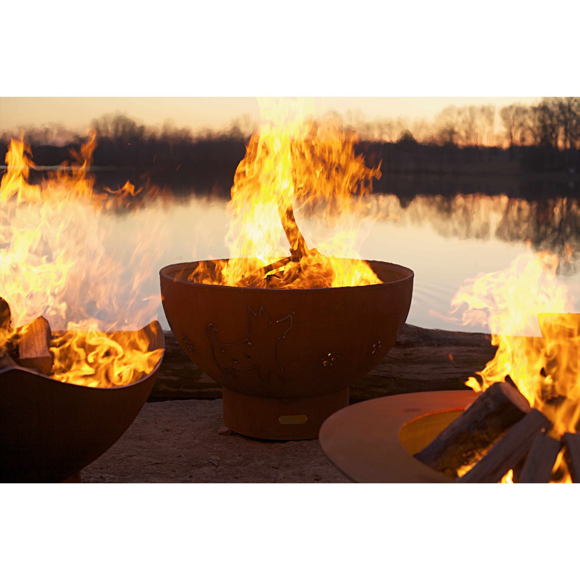 Three fire pits with flames burning near a body of water during sunset.