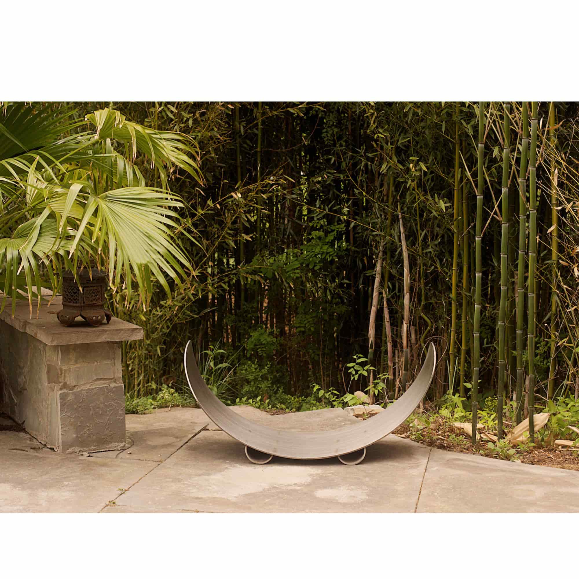 Carbon steel wood log rack in a garden setting with greenery