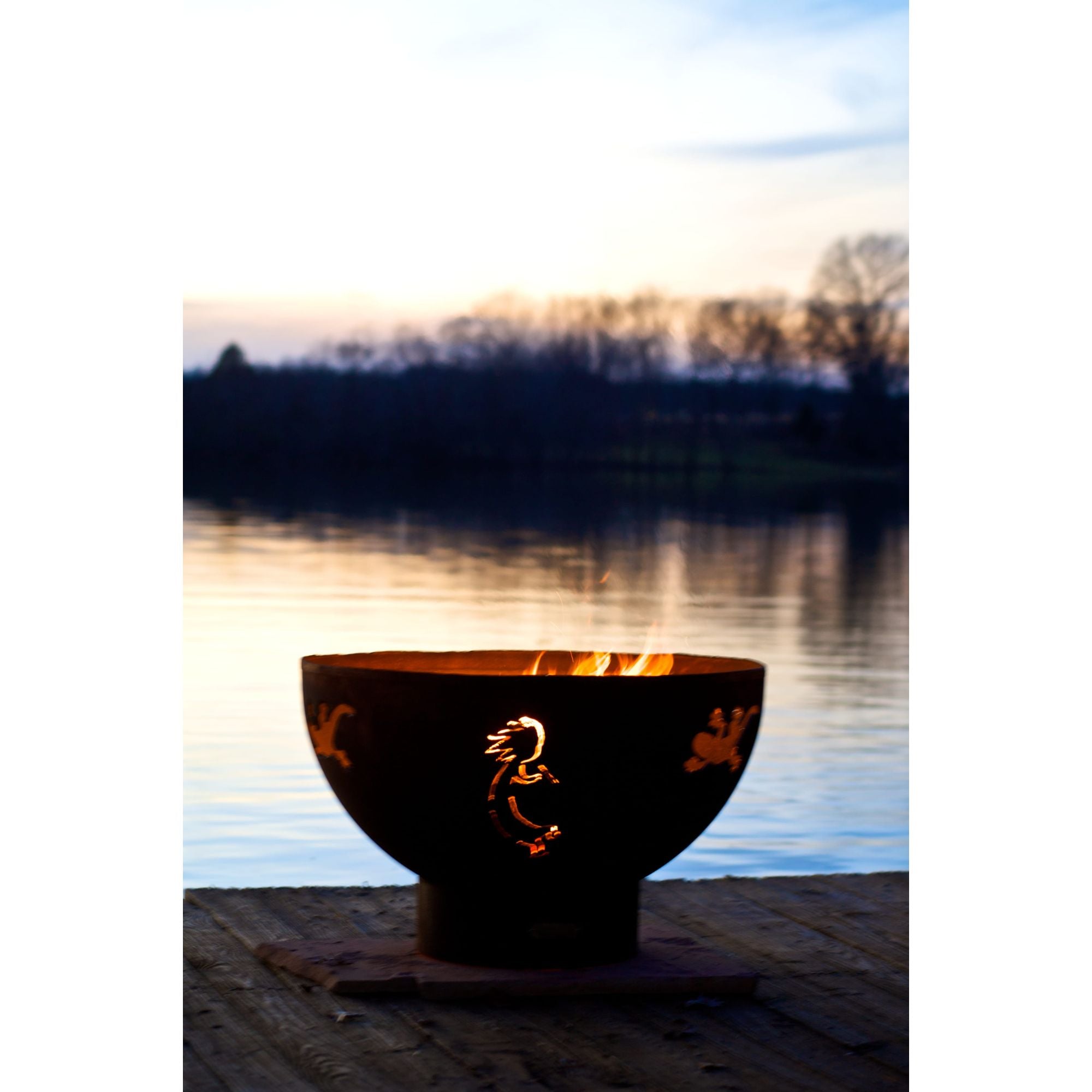 Fire pit bowl with flames on a dock by a lake at sunset
