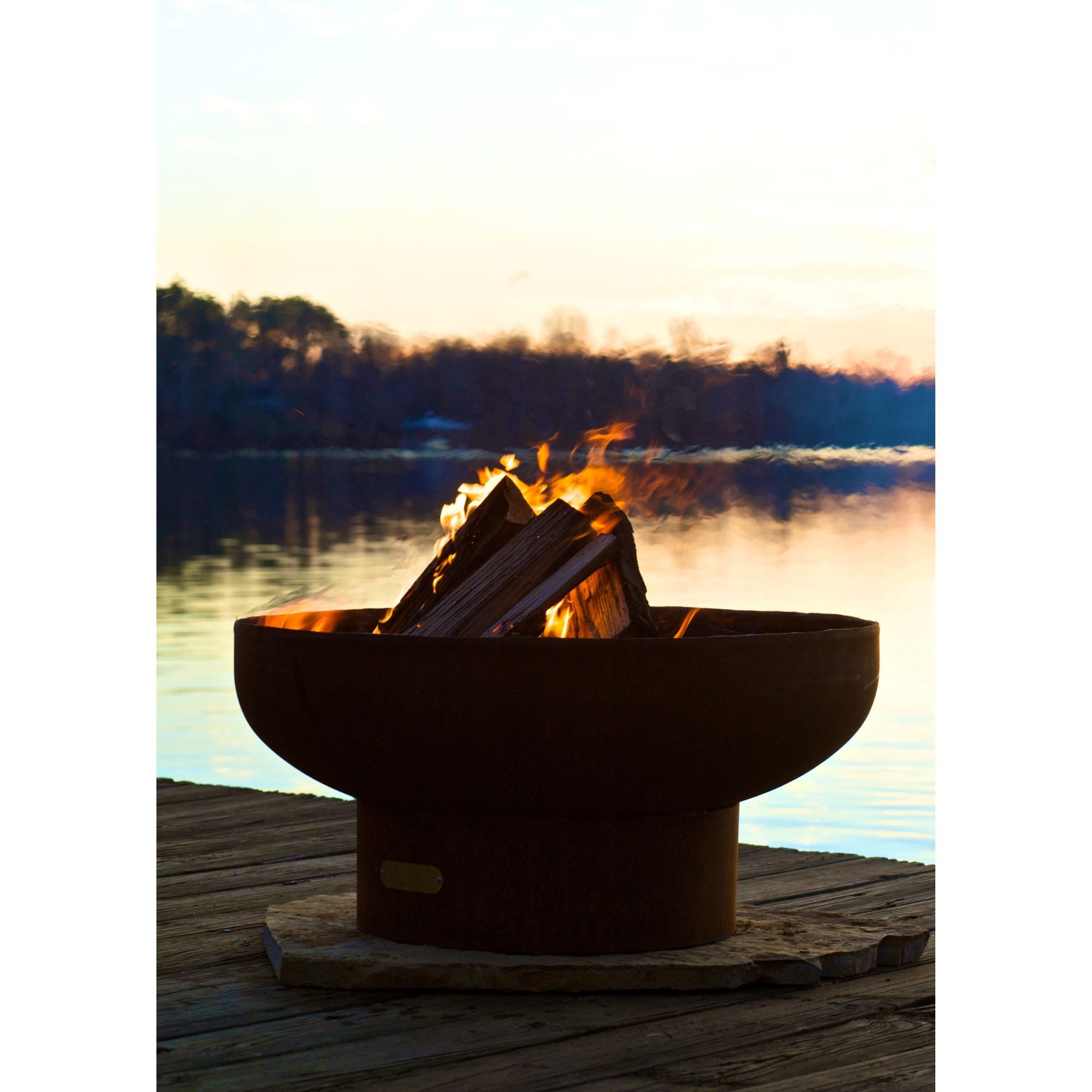Fire pit with burning wood on a dock by a lake at sunset
