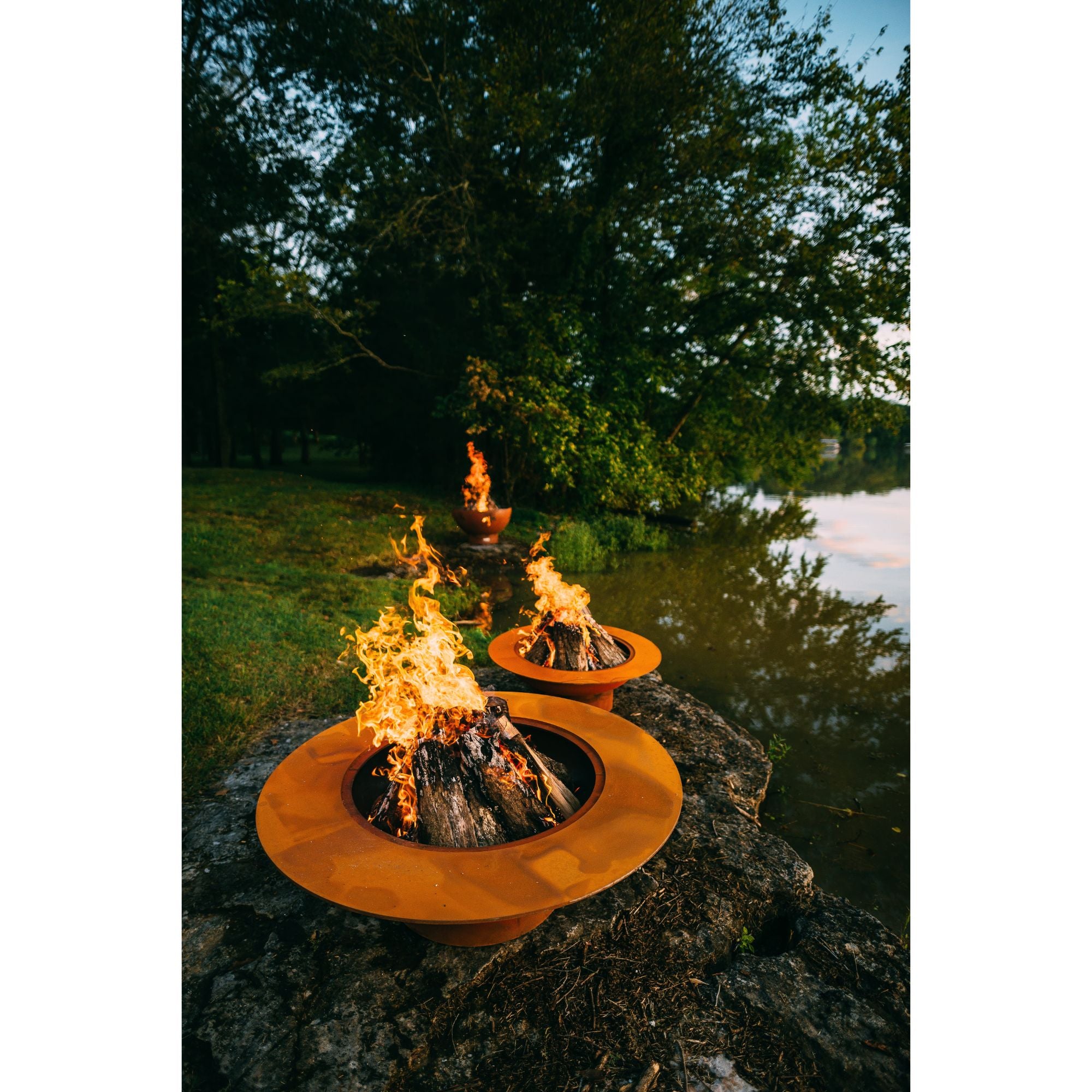 Two fire pits on rocks by a body of water with trees in the background