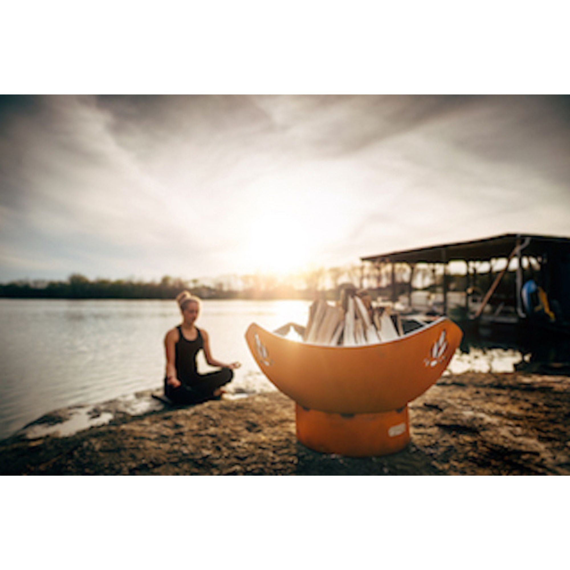 Person meditating by a lake with an orange fire pit on the shore.