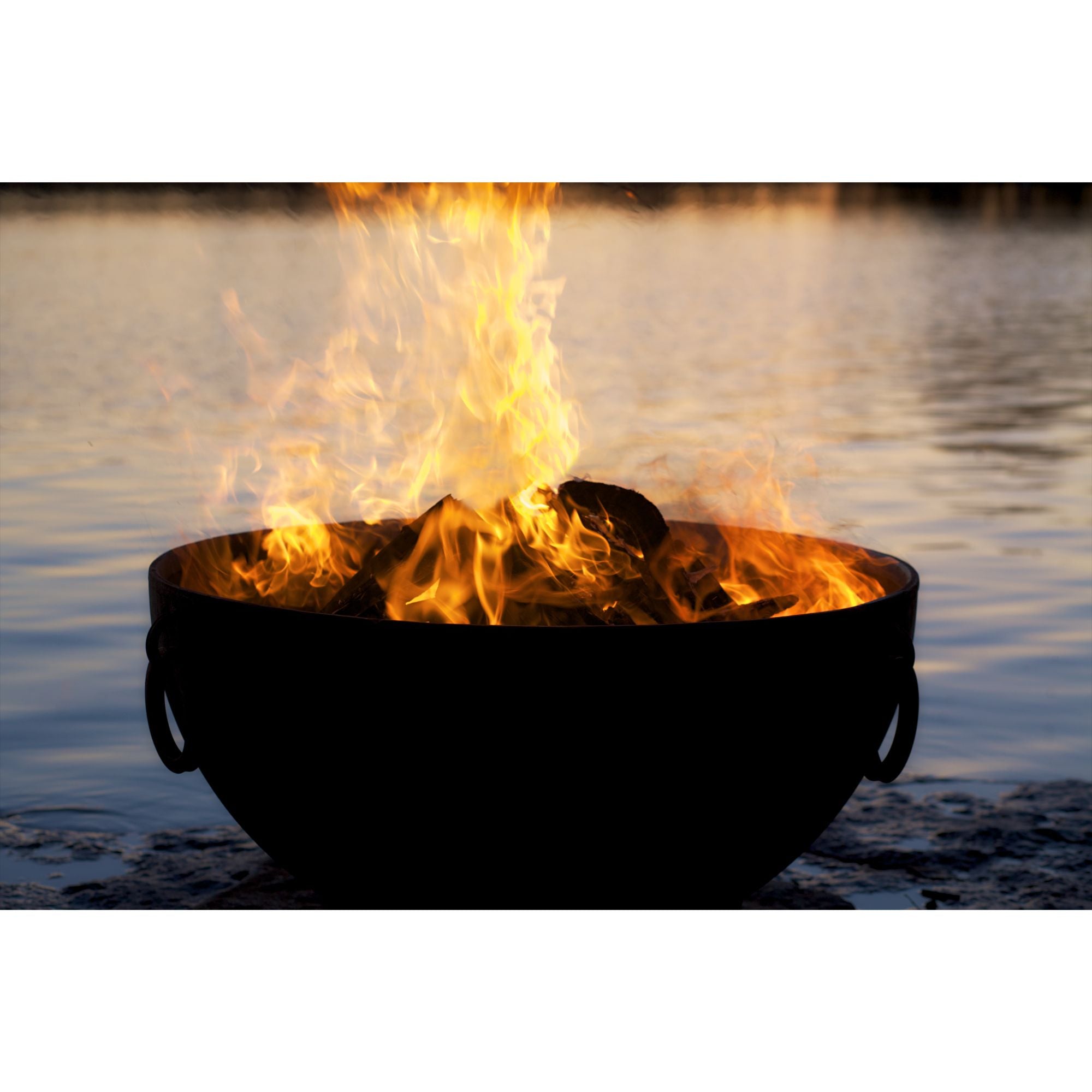 Fire pit with flames burning brightly in a bowl by a body of water.