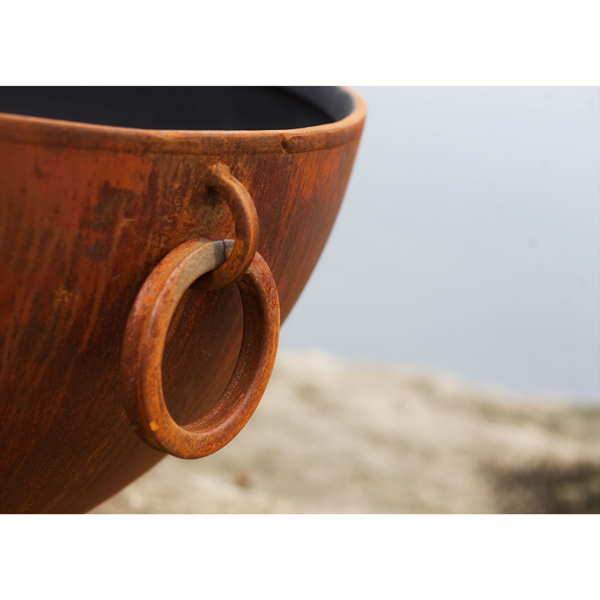 rusty fire pit bowl with circular handles on a sandy surface