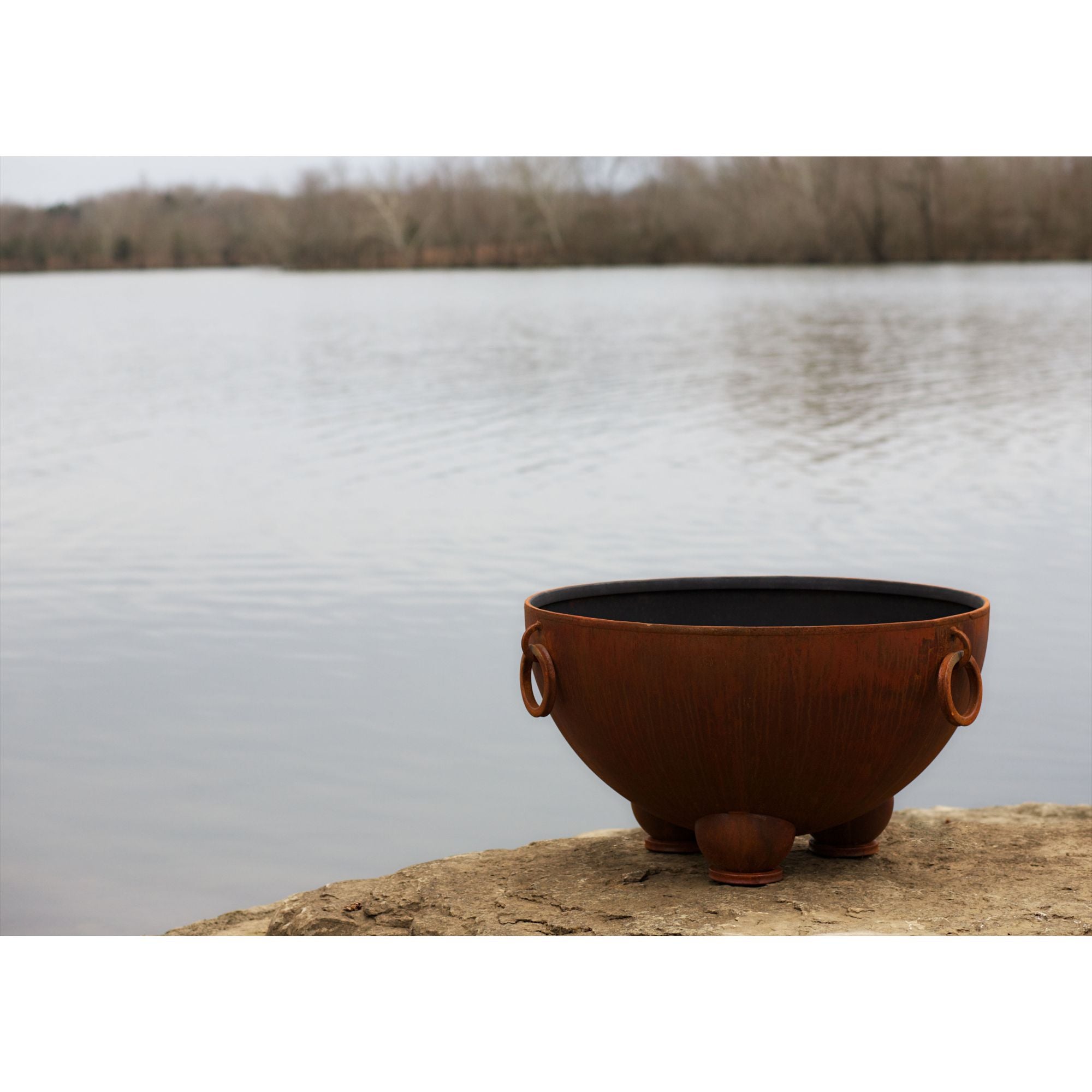 Rust-colored metal fire pit on a rock by a lake
