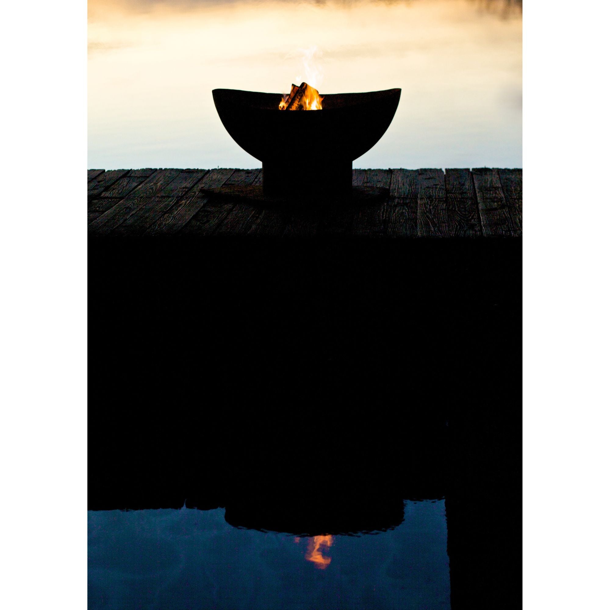 Fire pit on a dock with water reflection at sunset