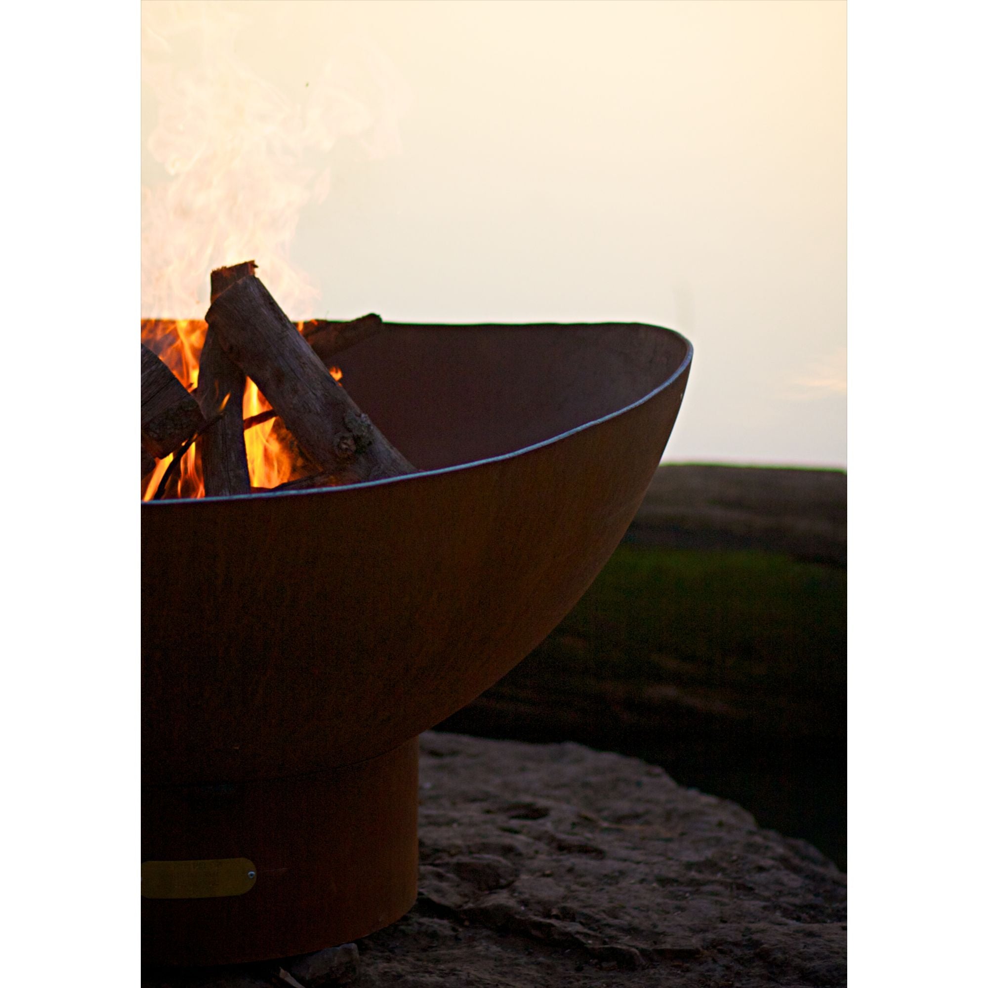 Fire pit with burning logs on a rocky surface during sunset.