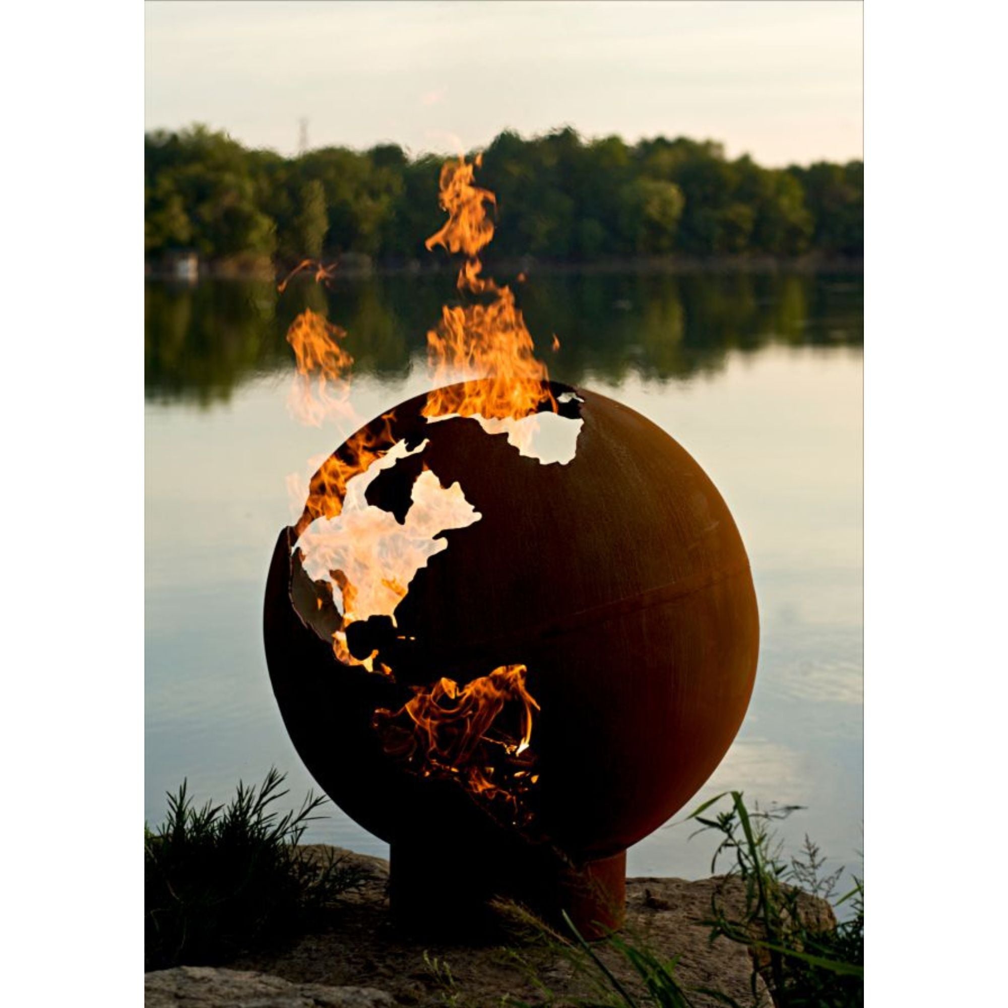 Spherical fire pit with flames against a lake and trees background