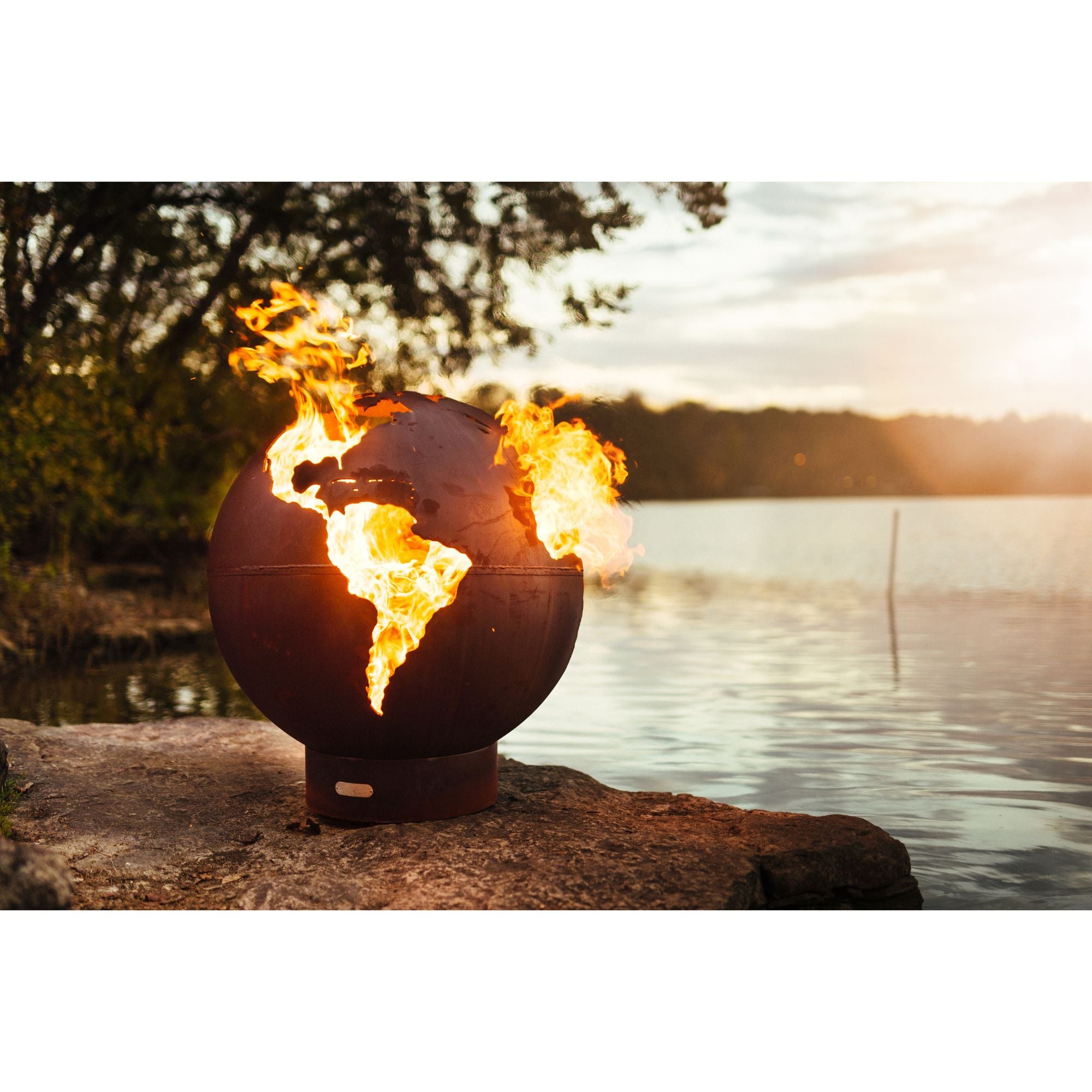 Fire pit shaped like the world with flames at sunset by a lake
