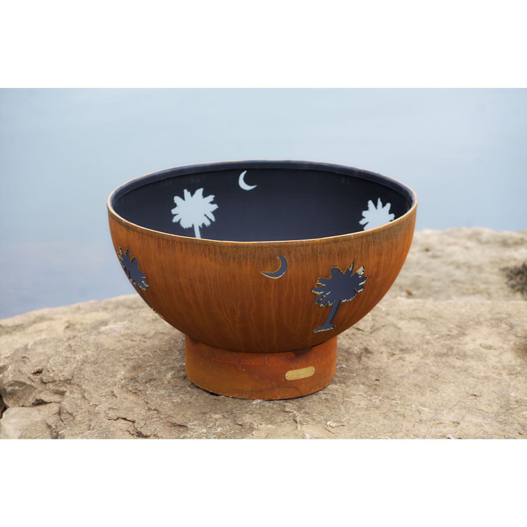 Decorative fire bowl with palm tree and moon designs on a rock surface