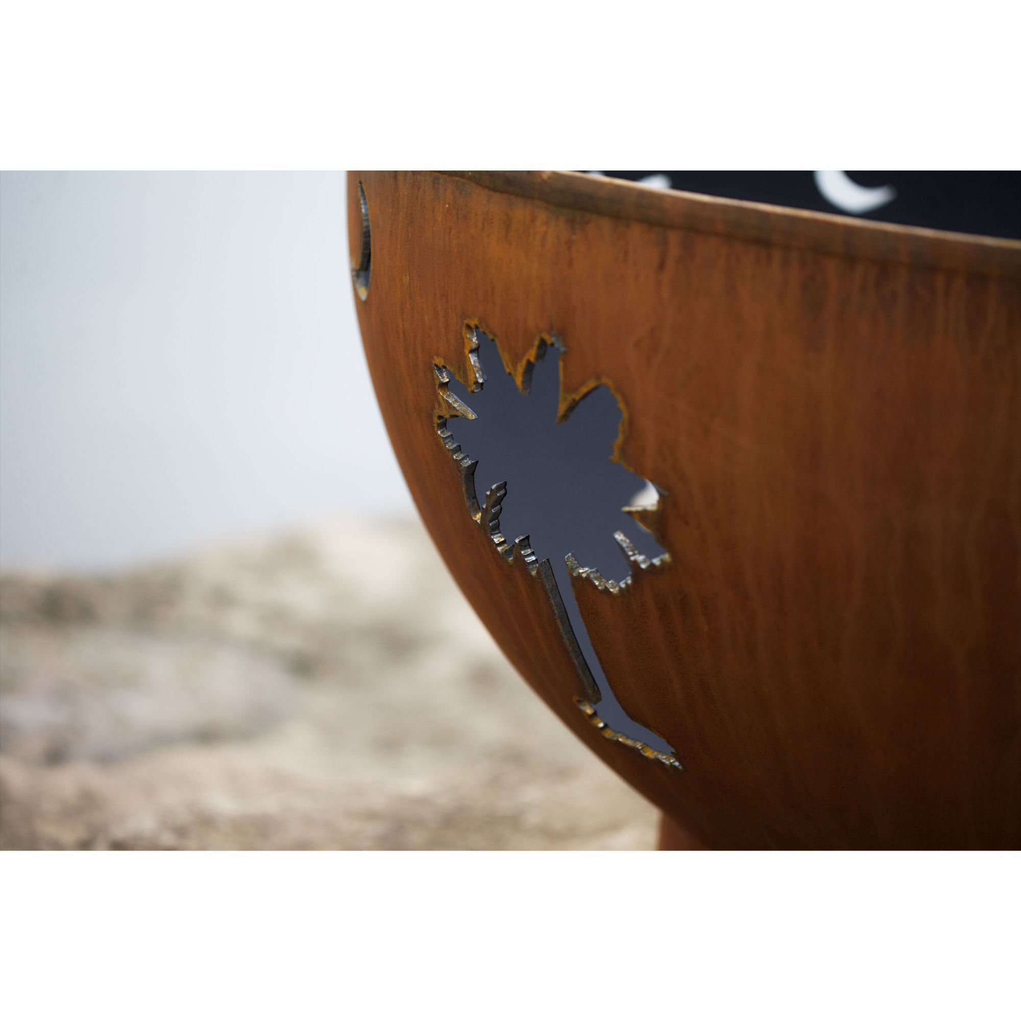 Rust-colored metal fire pit with palm tree design on a blurred natural background