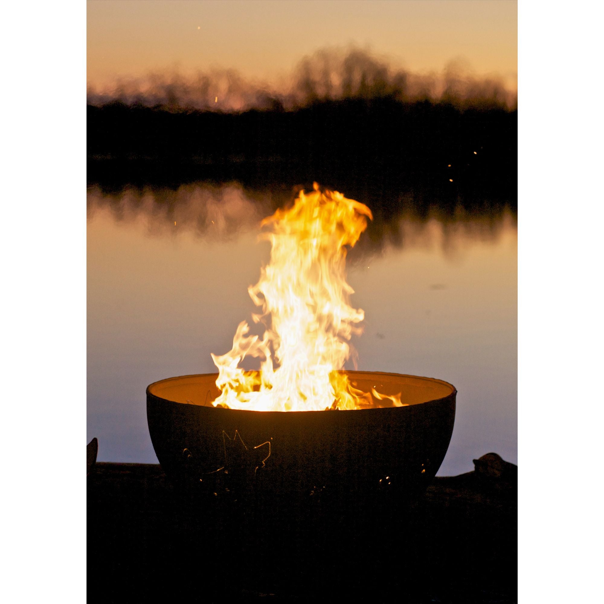 Fire pit with flames glowing brightly against a sunset over water backdrop