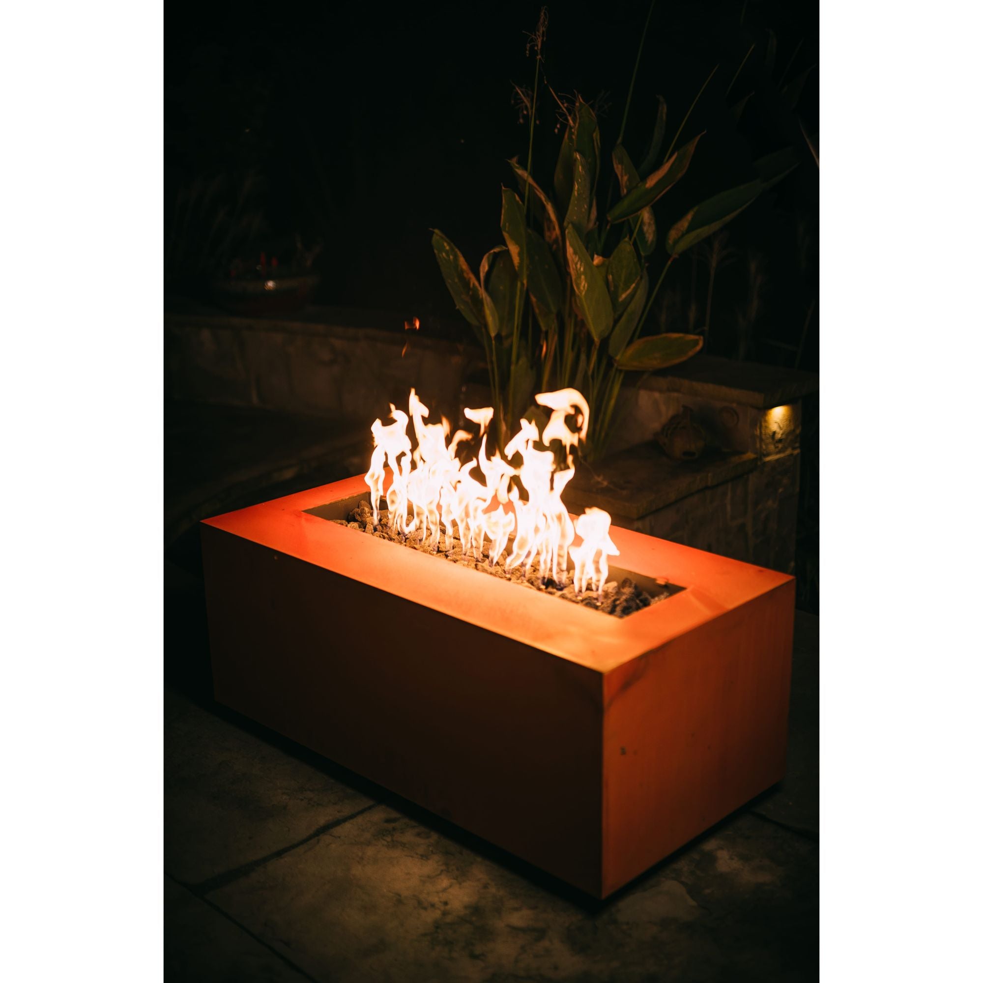 Rectangular fire pit with flames glowing in a dark outdoor setting