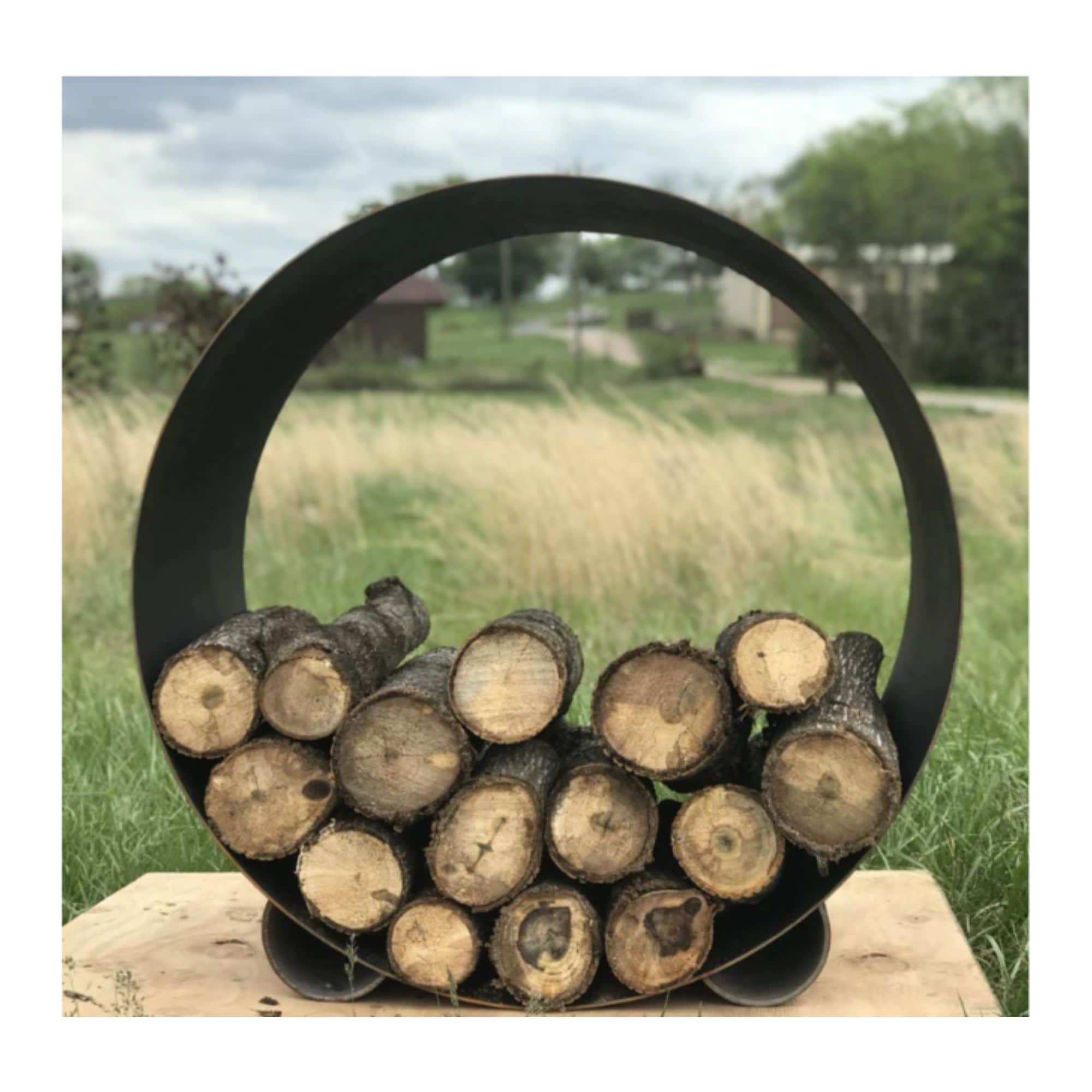 Black round steel firewood holder with logs against a natural background