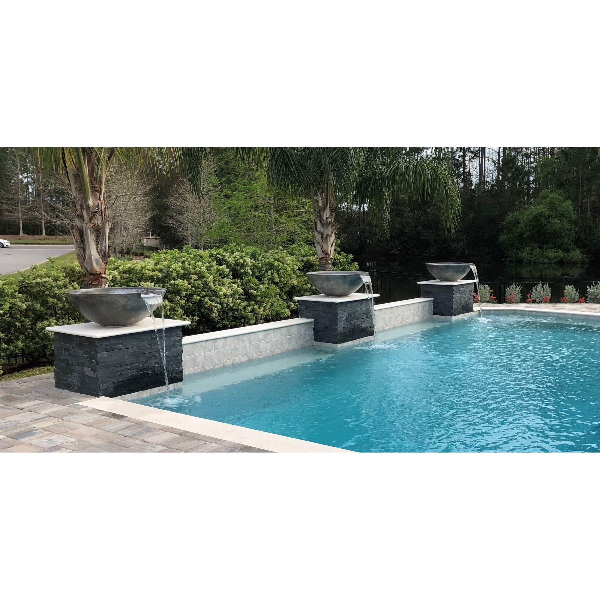 fire on water bowl with a water scupper, by a pool, with trees in the background