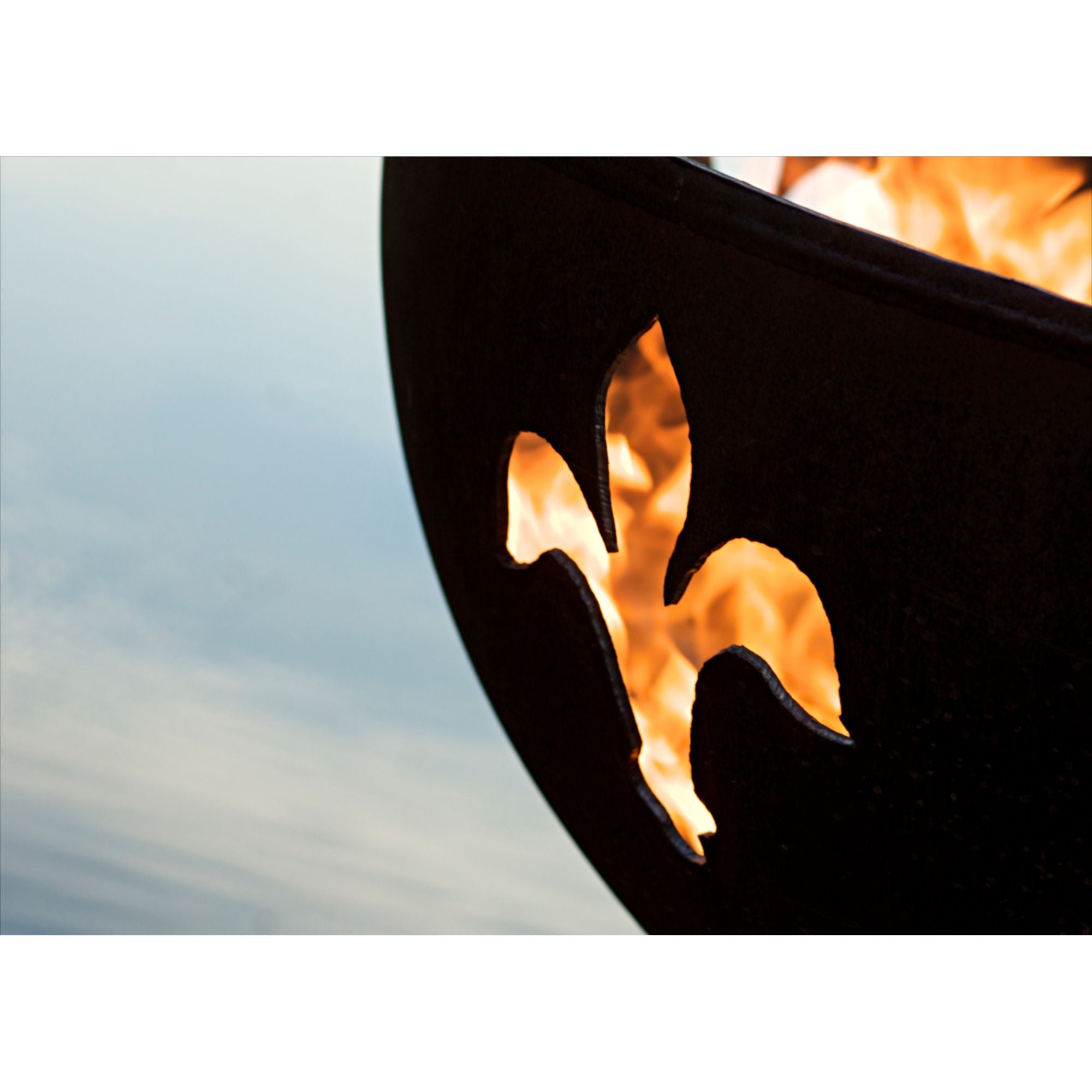 Close-up of a fire pit with flames and a blurred sky background