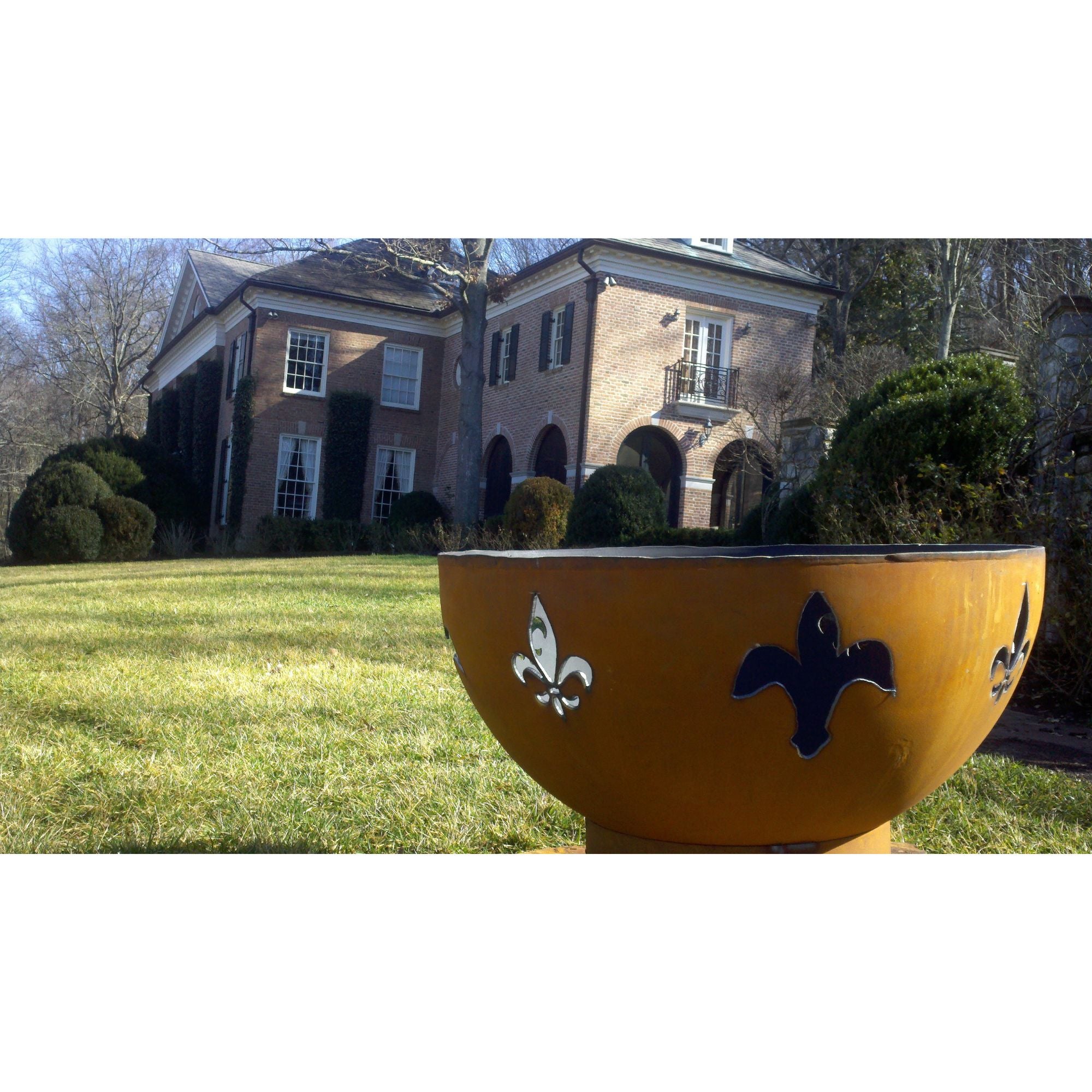 Yellow fire pit with fleur-de-lis designs in front of a brick house.