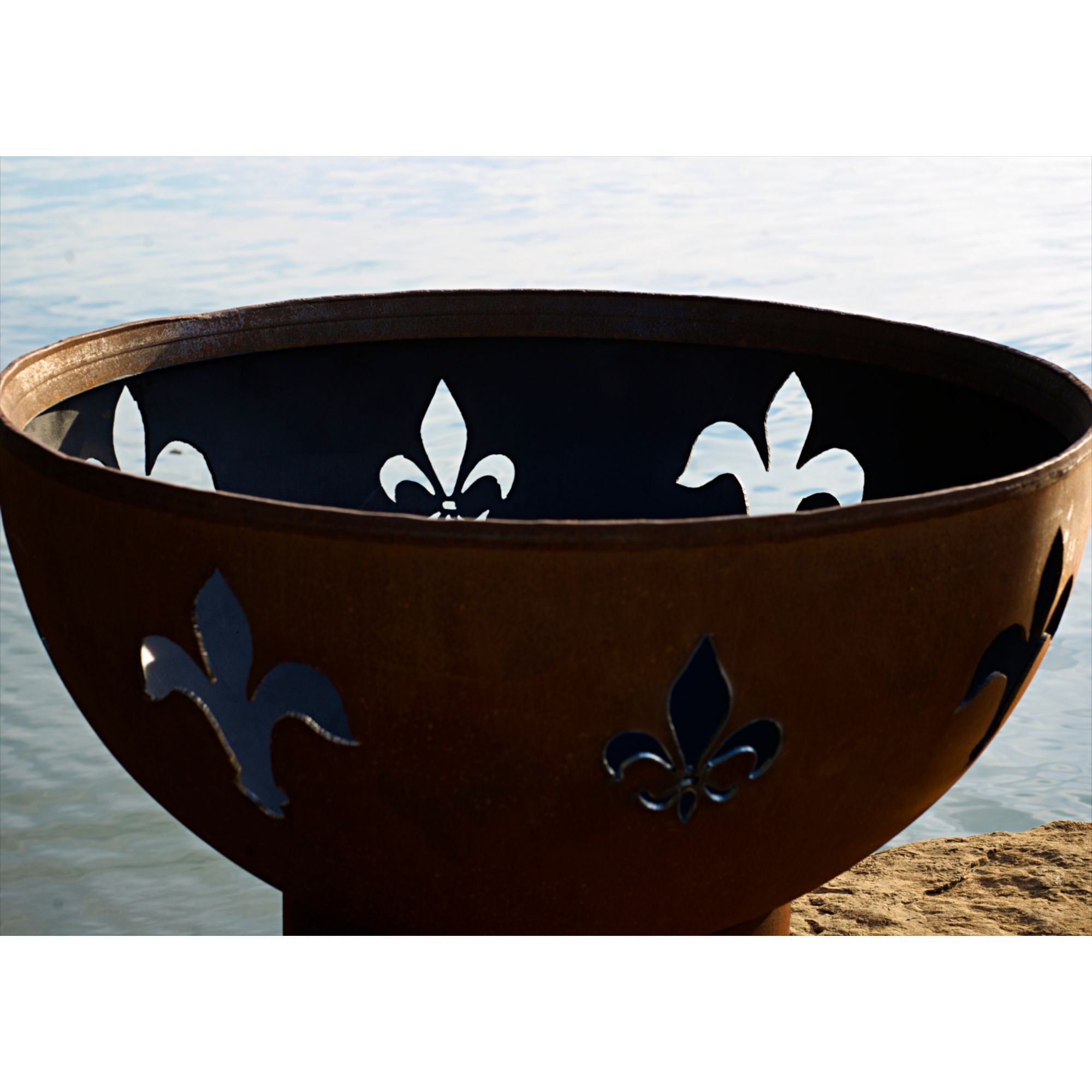 Decorative fire pit with fleur-de-lis designs against a water background