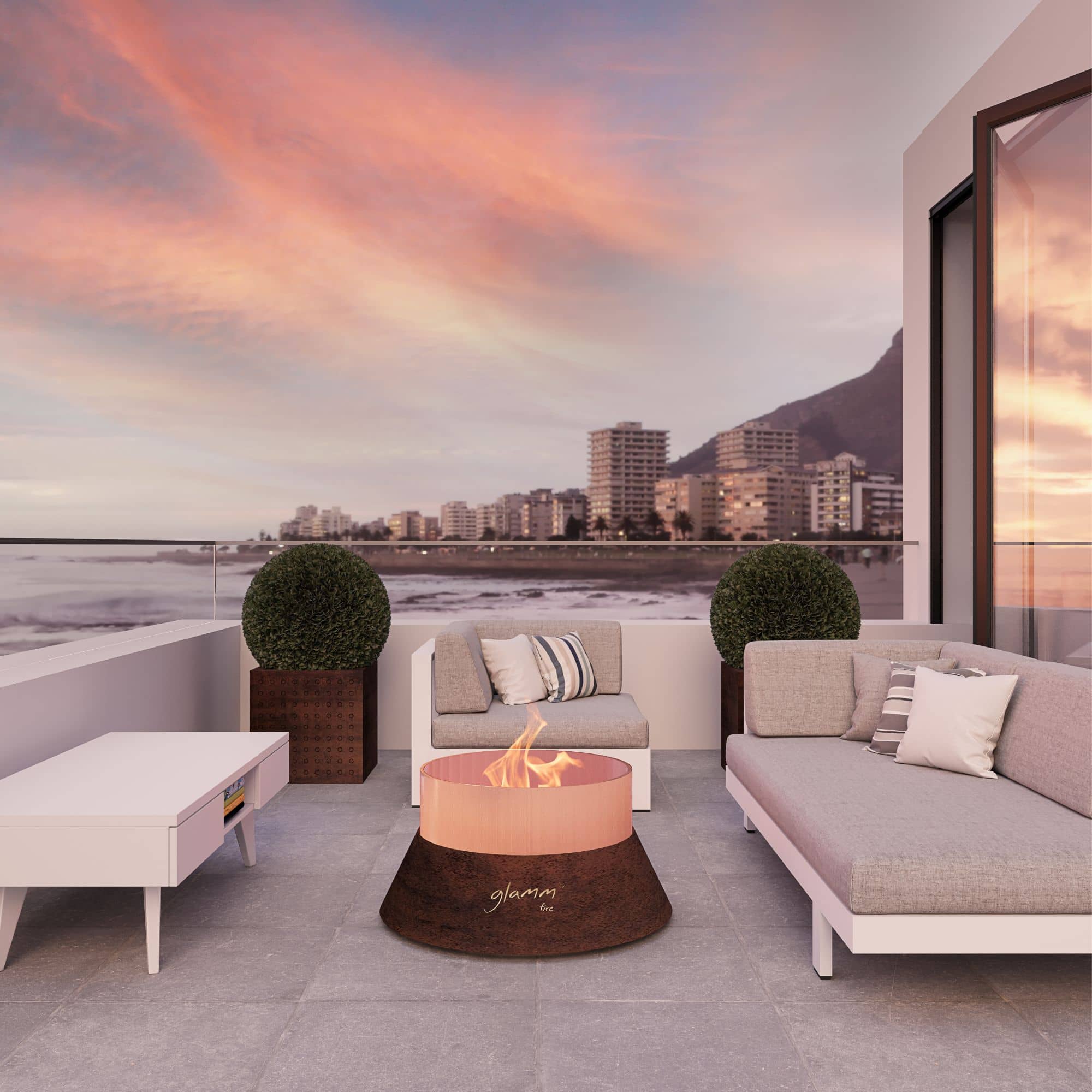 fire pit with flames standing outside on a rock patio with a sofa, by the ocean