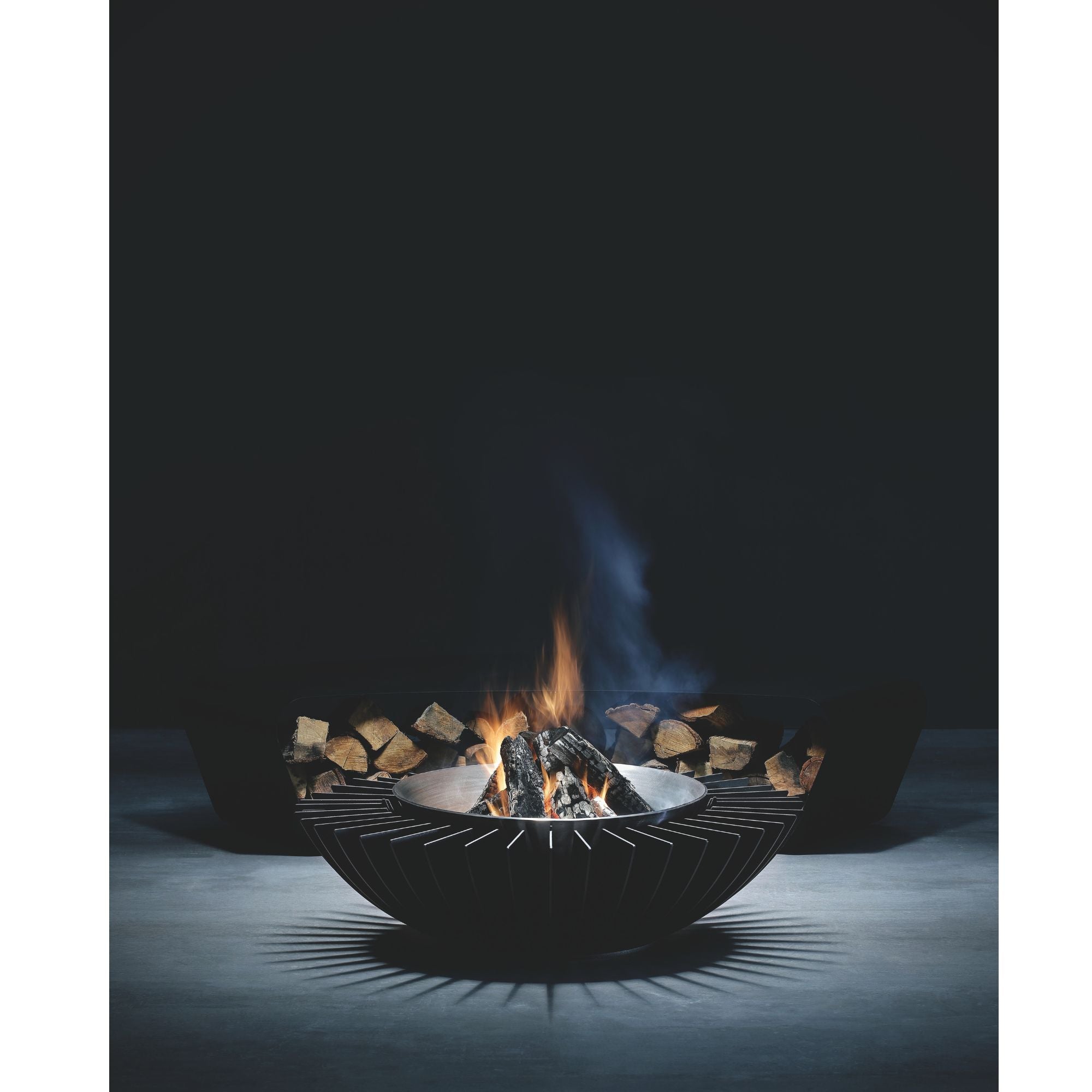 Modern outdoor fire pit with flames and logs on a dark background