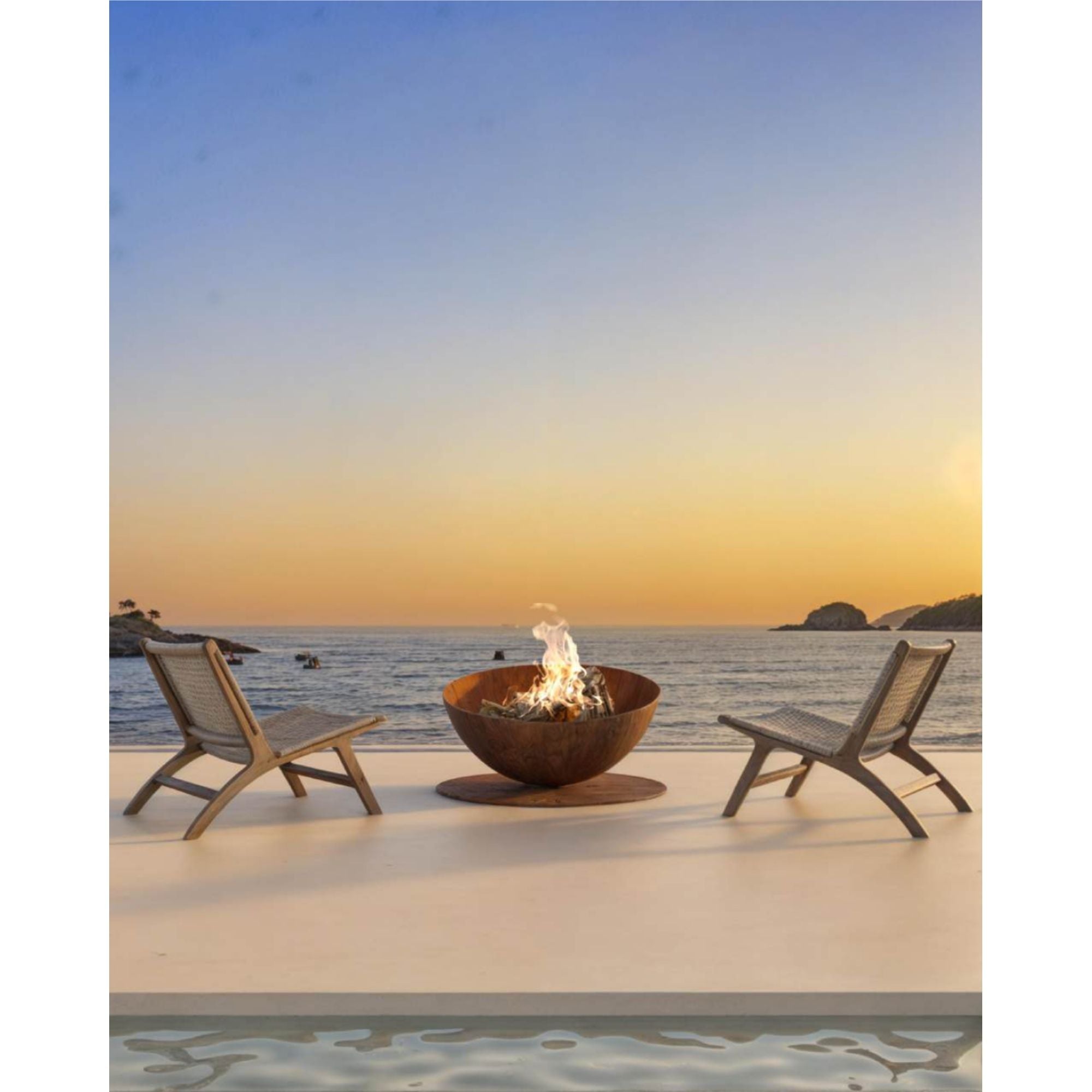 Two chairs around a fire pit on a beach at sunset.