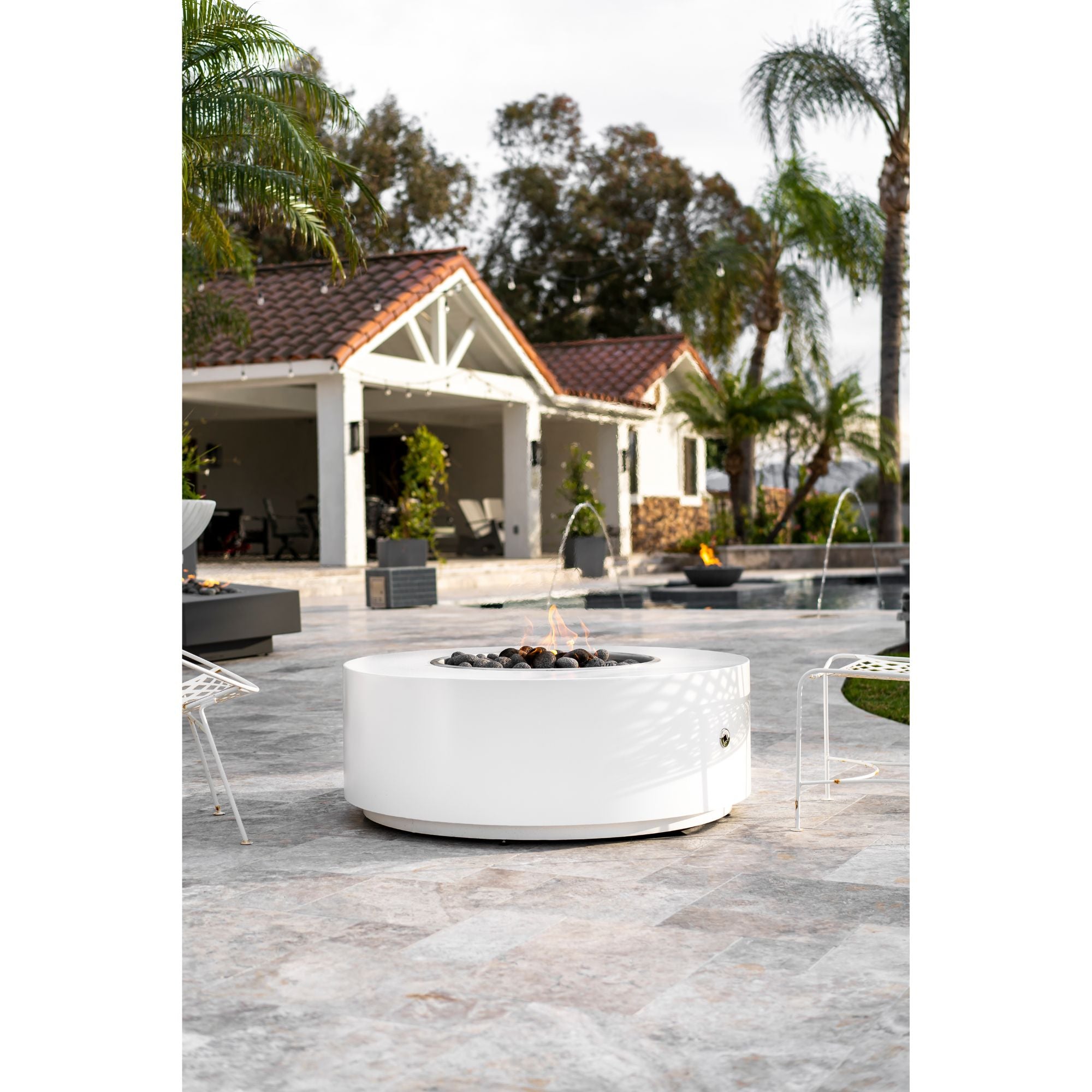white round firepit with flames in an outdoor setting with trees.