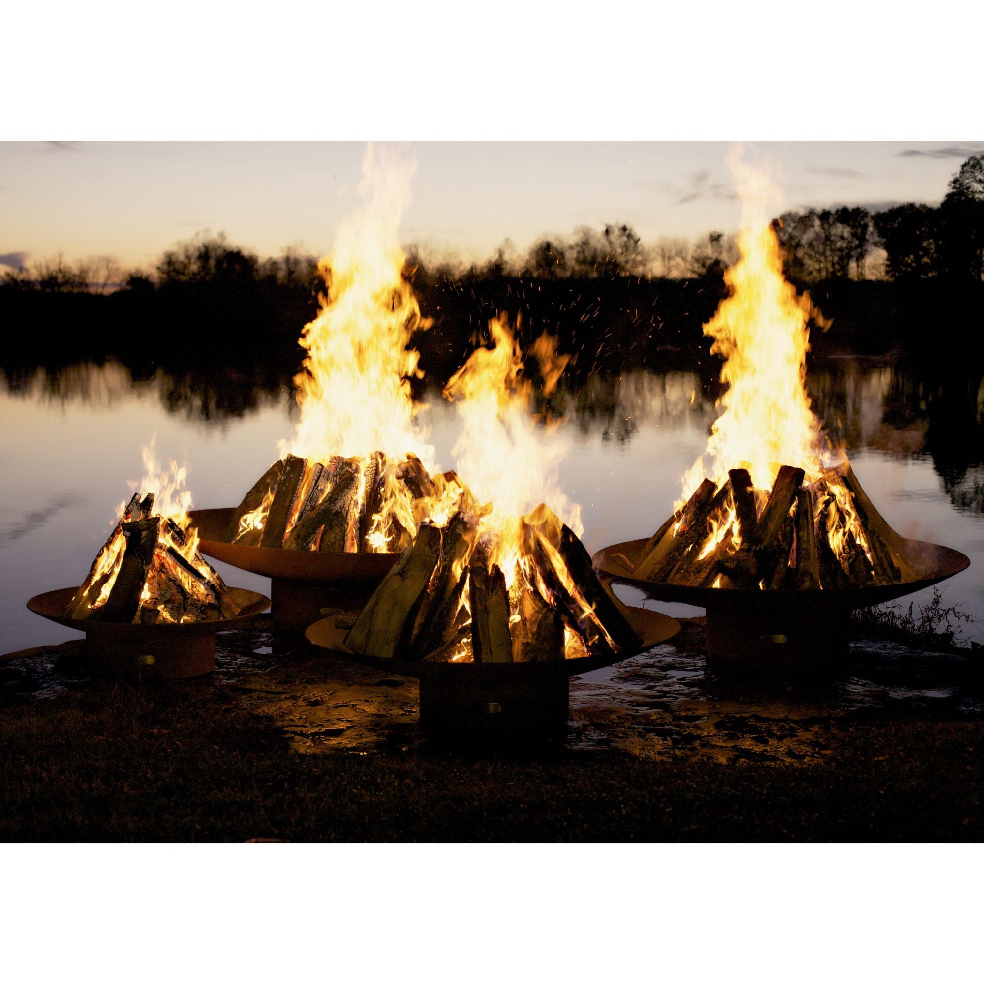Three fire pits with flames burning near a body of water during sunset.