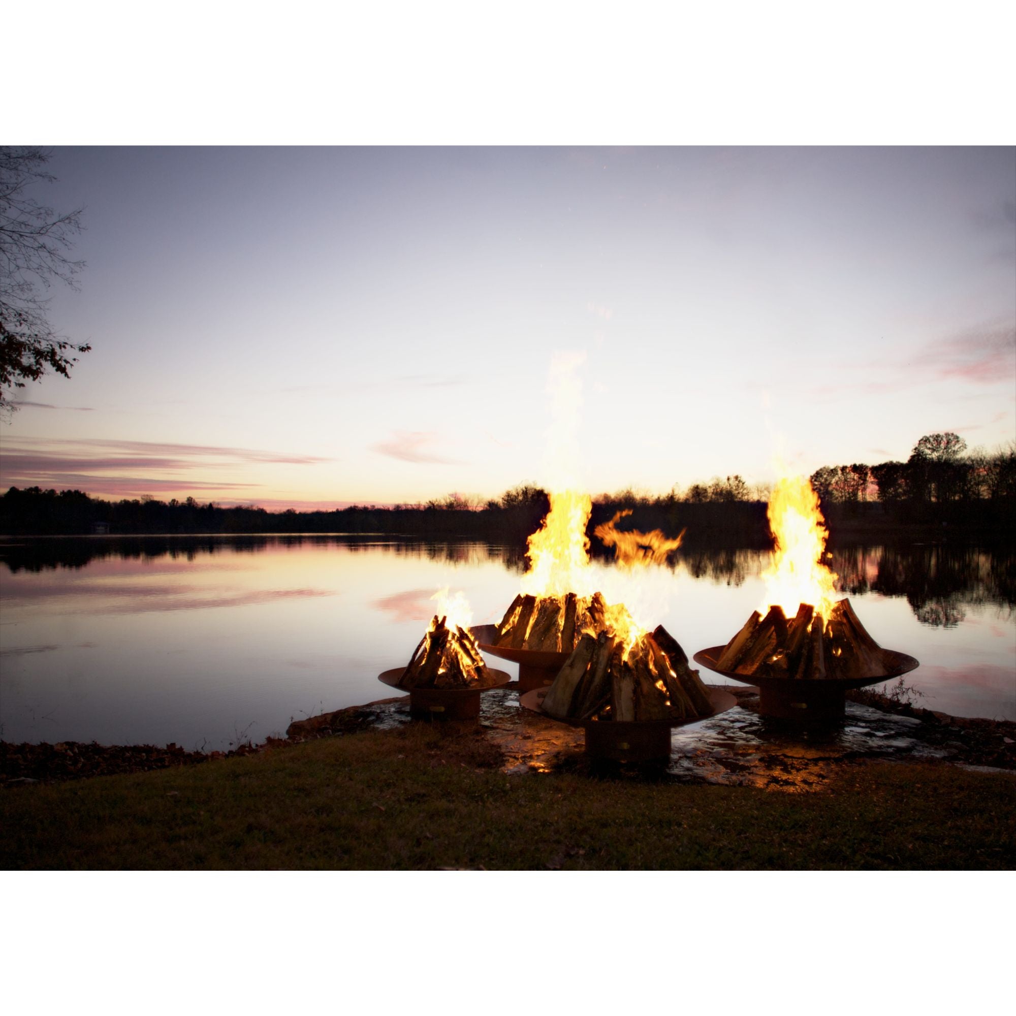 Fire pit by a lake at sunset with flames reflecting on the water.