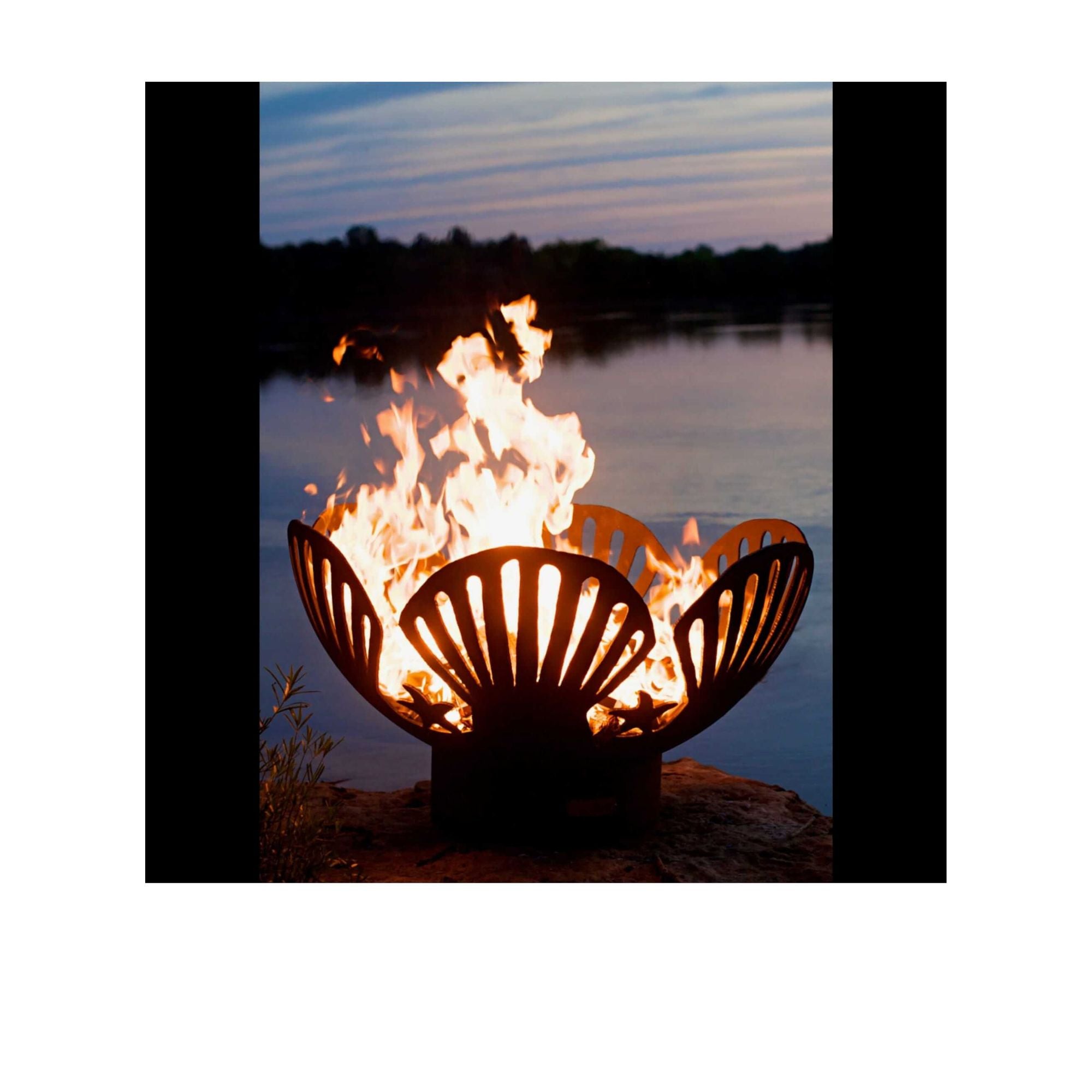 Fire pit with flames burning in front of a lake at sunset