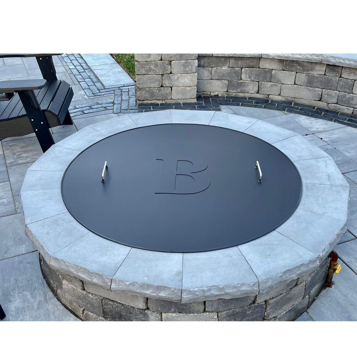 Master Flame one piece round fire pit cover on a stone fire pit, shown with optional monogram