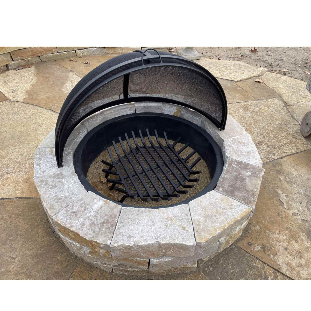 Master Flame round fire pit grate in a stone fire pit with a dome safety screen