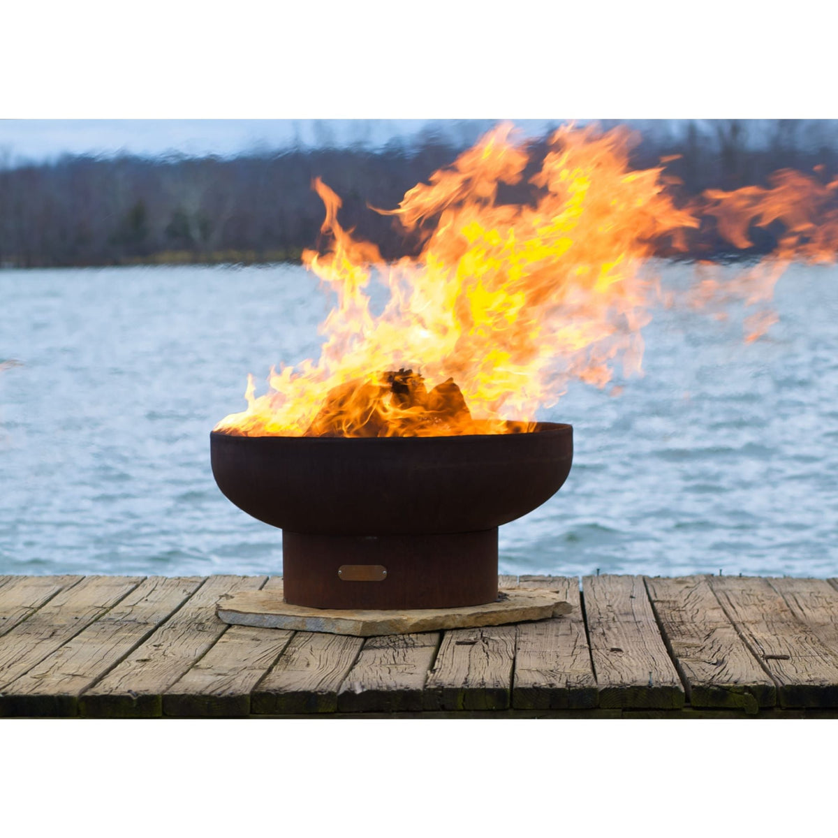 Low steel wood burning fire pit with tall flames on a lakeside deck