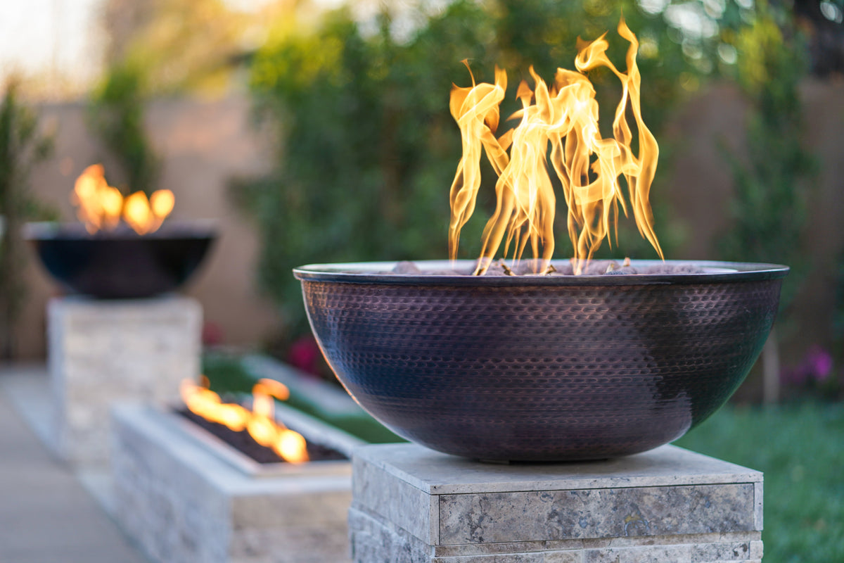 Copper gas fire bowl burning on a stone wall at dusk