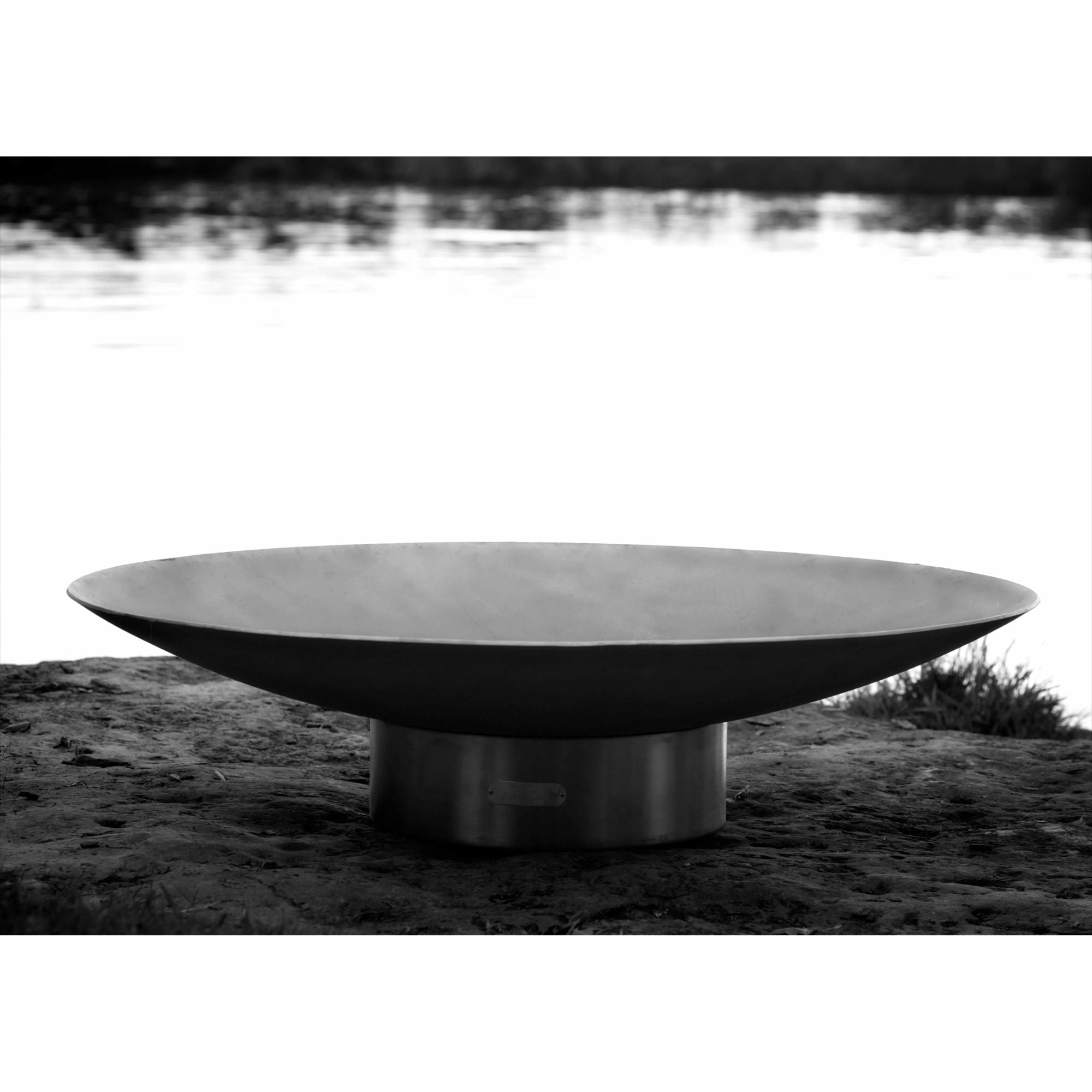 Large metal fire pit on a grassy area with water in the background