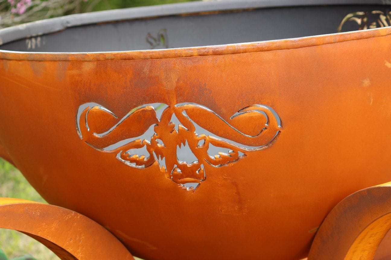 Rust-colored metal fire pit with bull head design on a blurred natural background