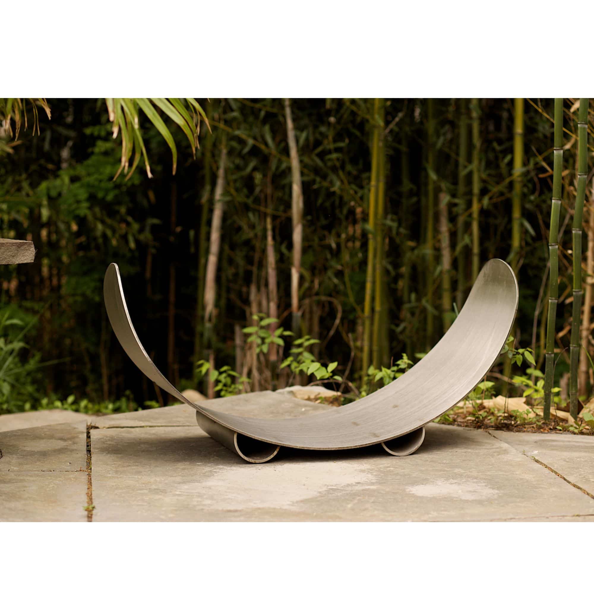 Carbon Steel wood log rack with curved design on a stone surface with a bamboo background