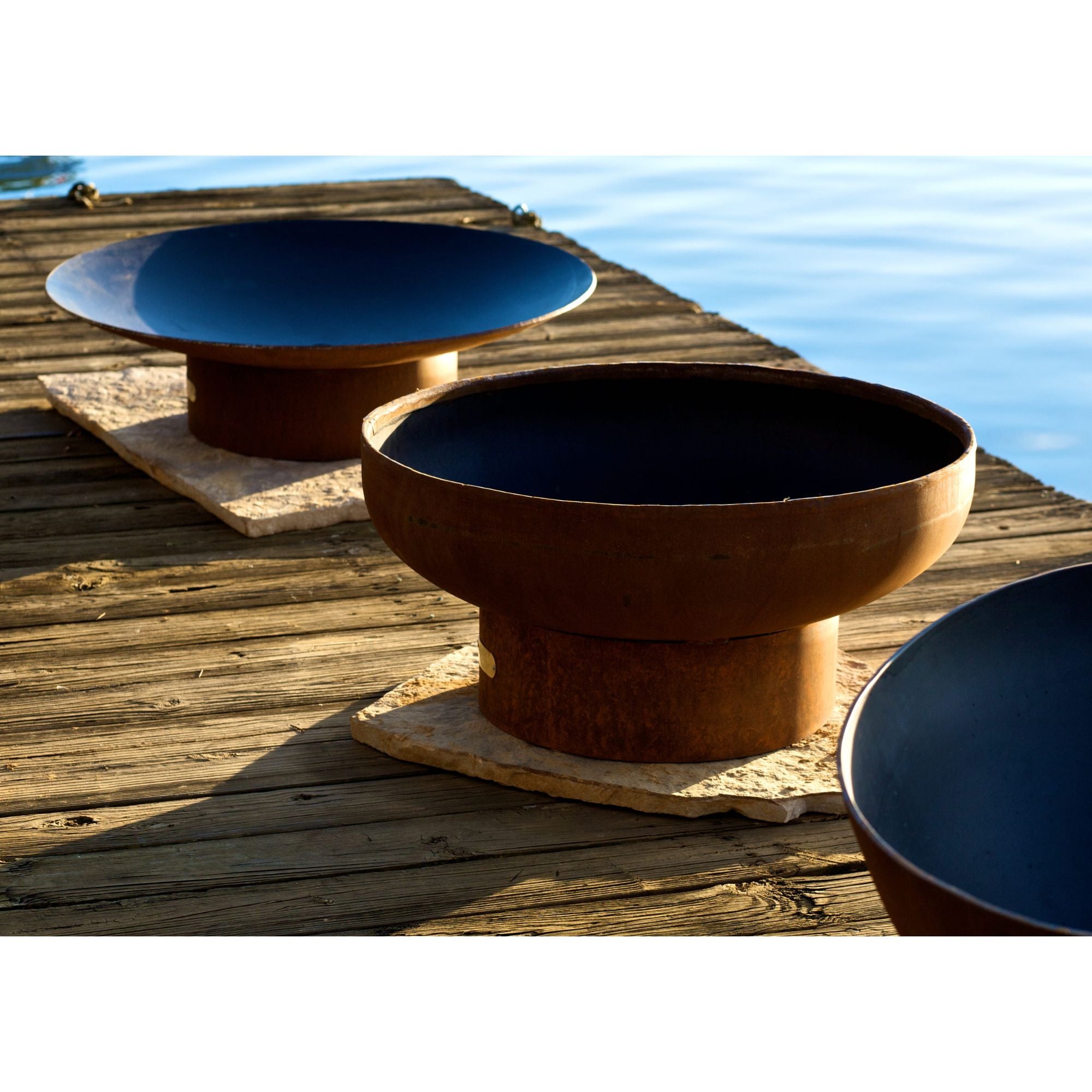Two metal bowls, one blue and one brown, on a wooden dock by a body of water.