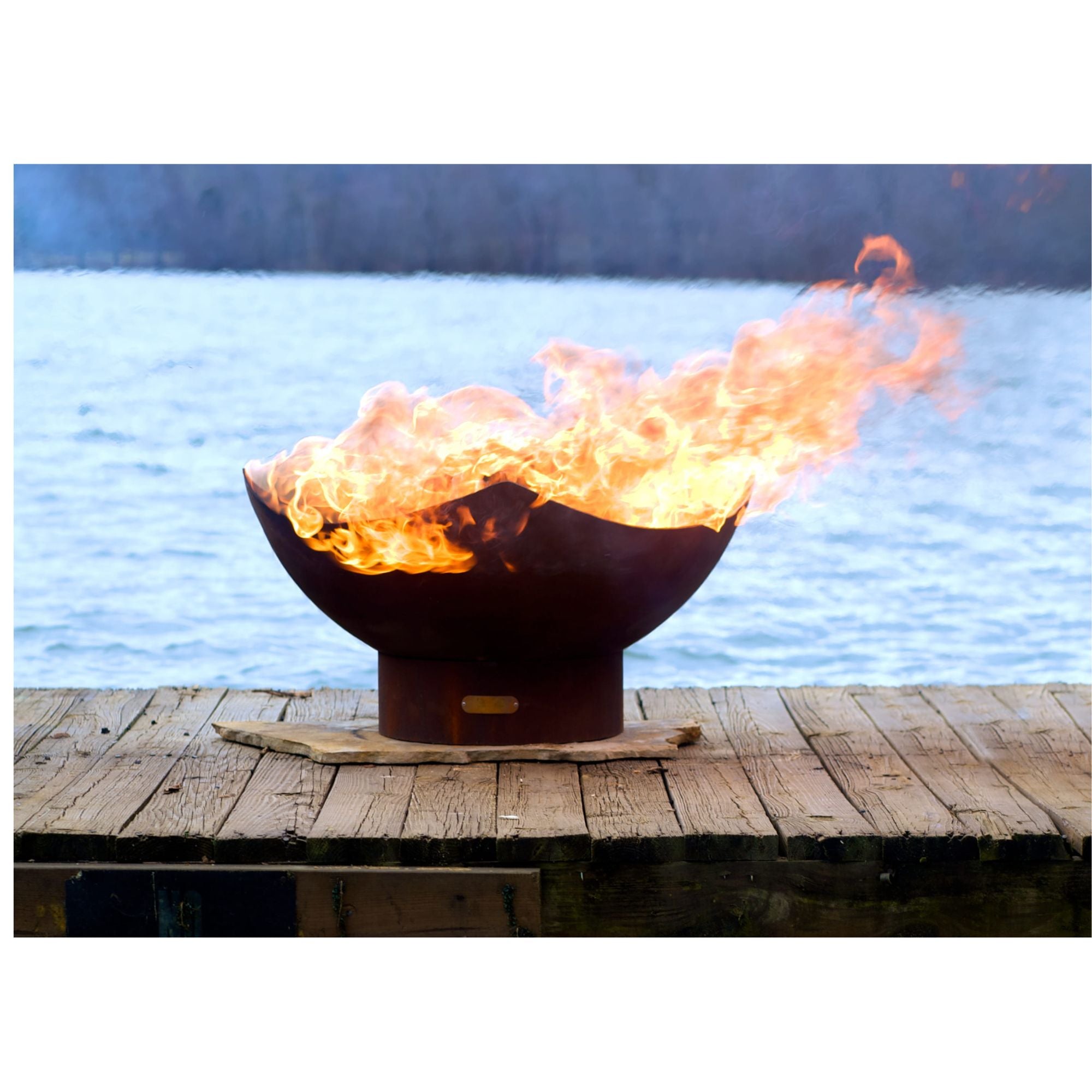Flaming fire pit on a wooden dock by a body of water