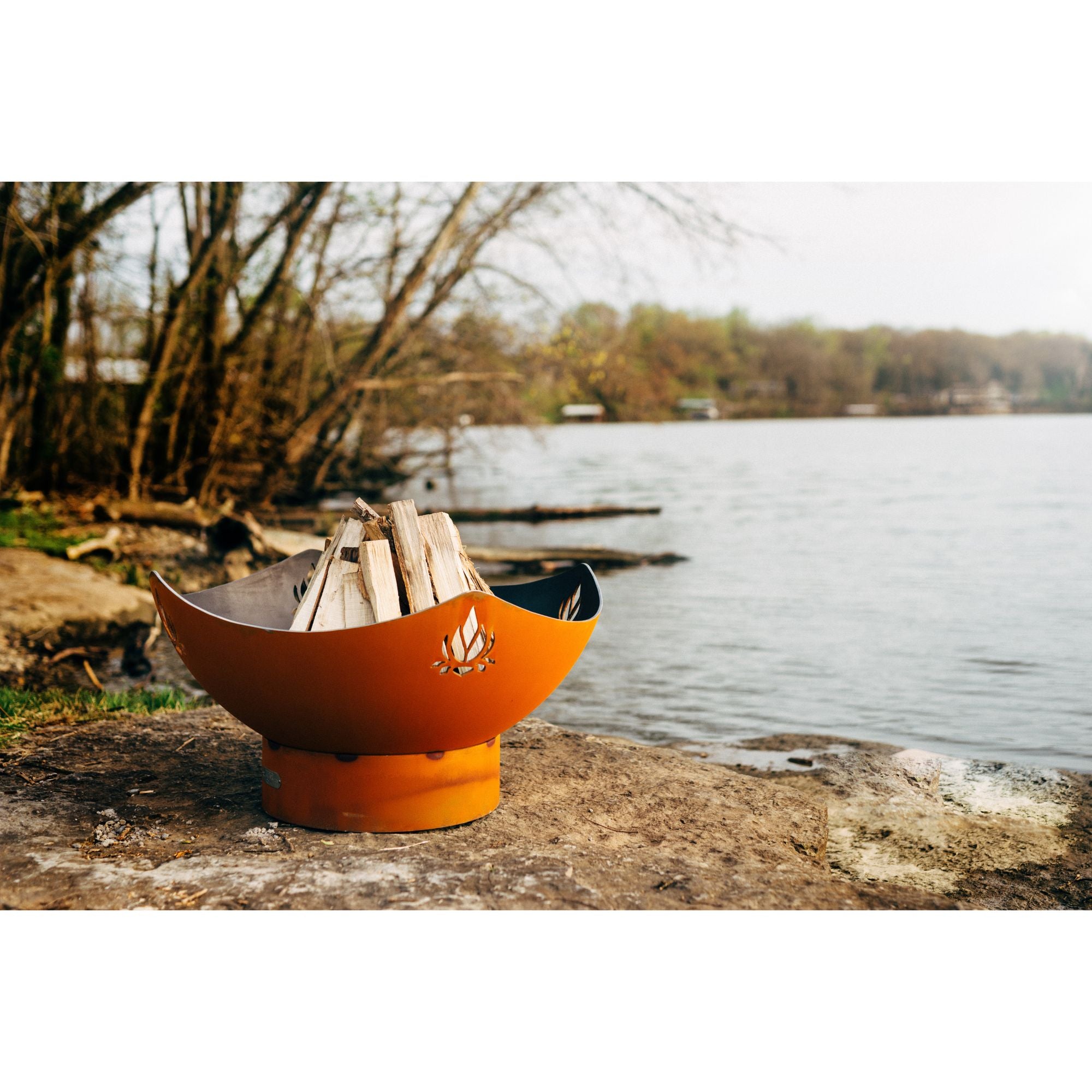 Orange fire pit with wooden logs on a lakeside setting