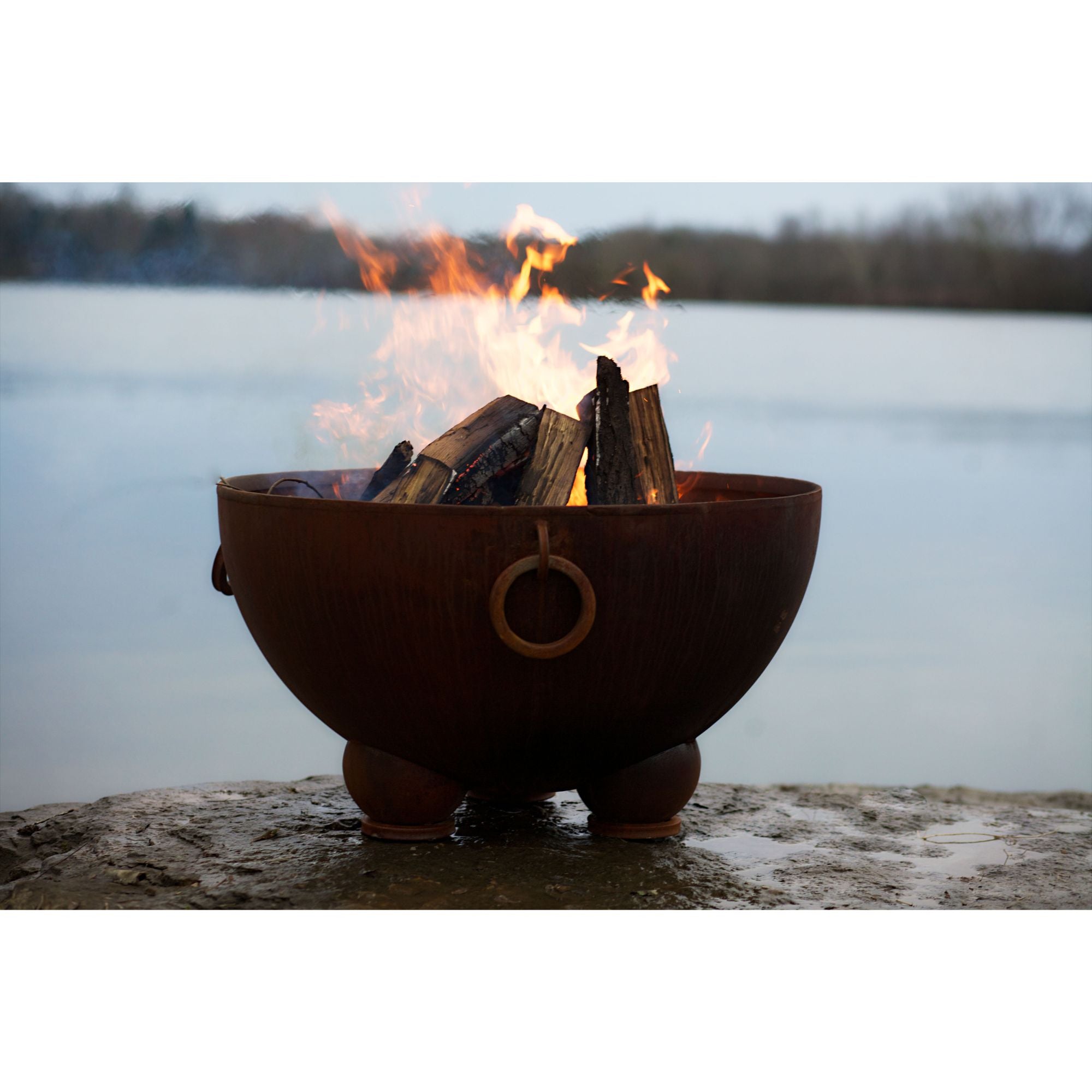 Fire pit with burning wood by a body of water