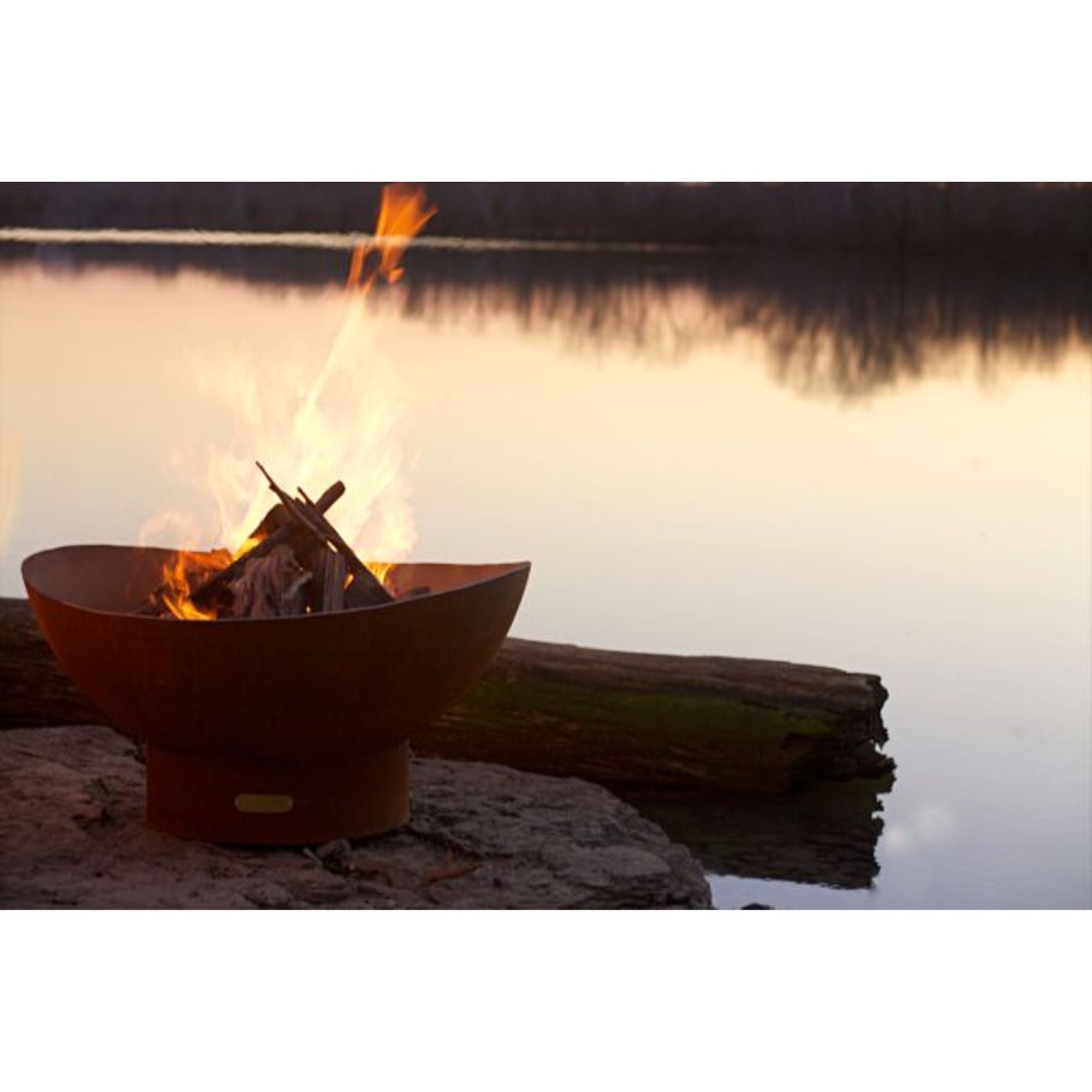 Fire pit with flames burning near a body of water at sunset