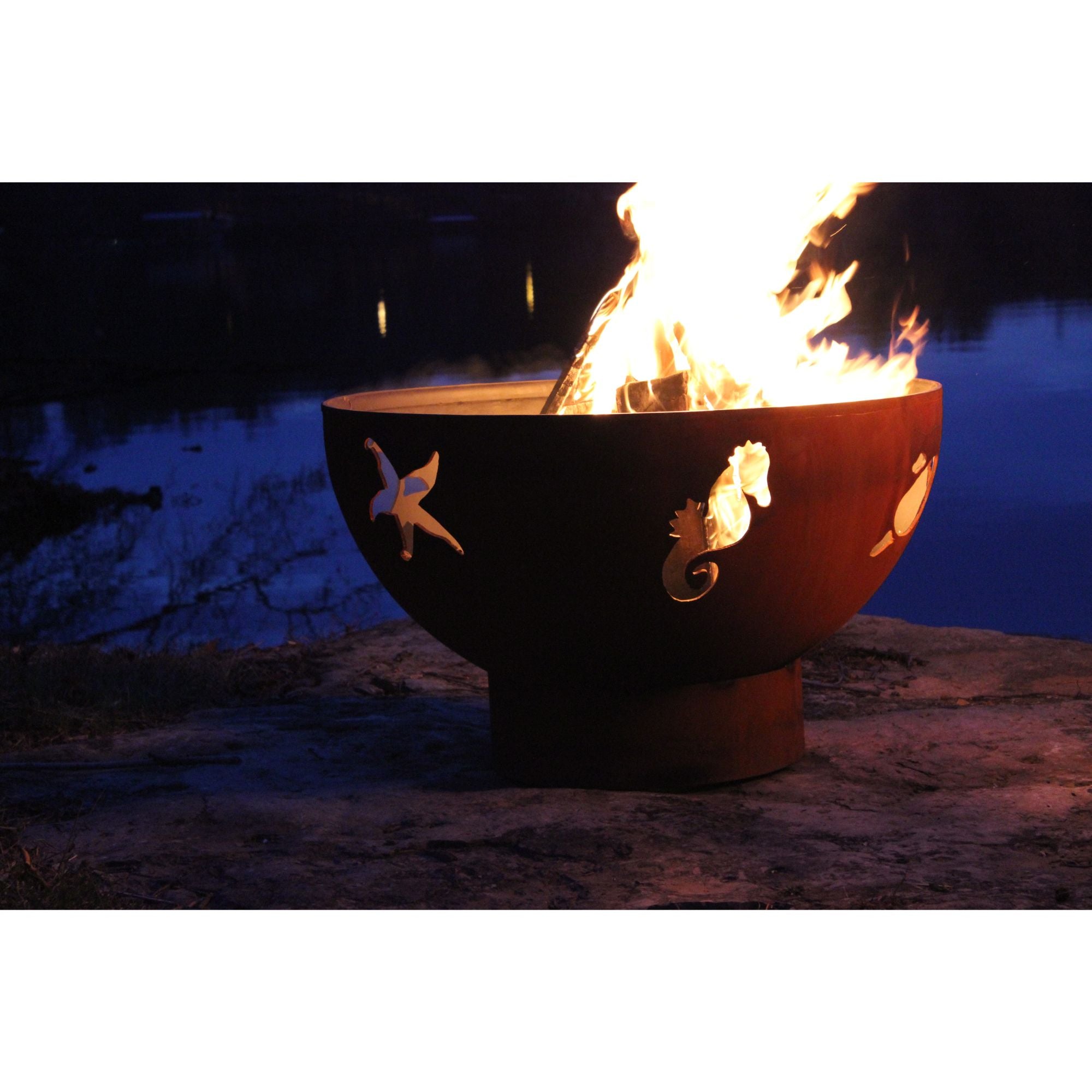 Fire pit with decorative seahorse designs by a body of water at night.
