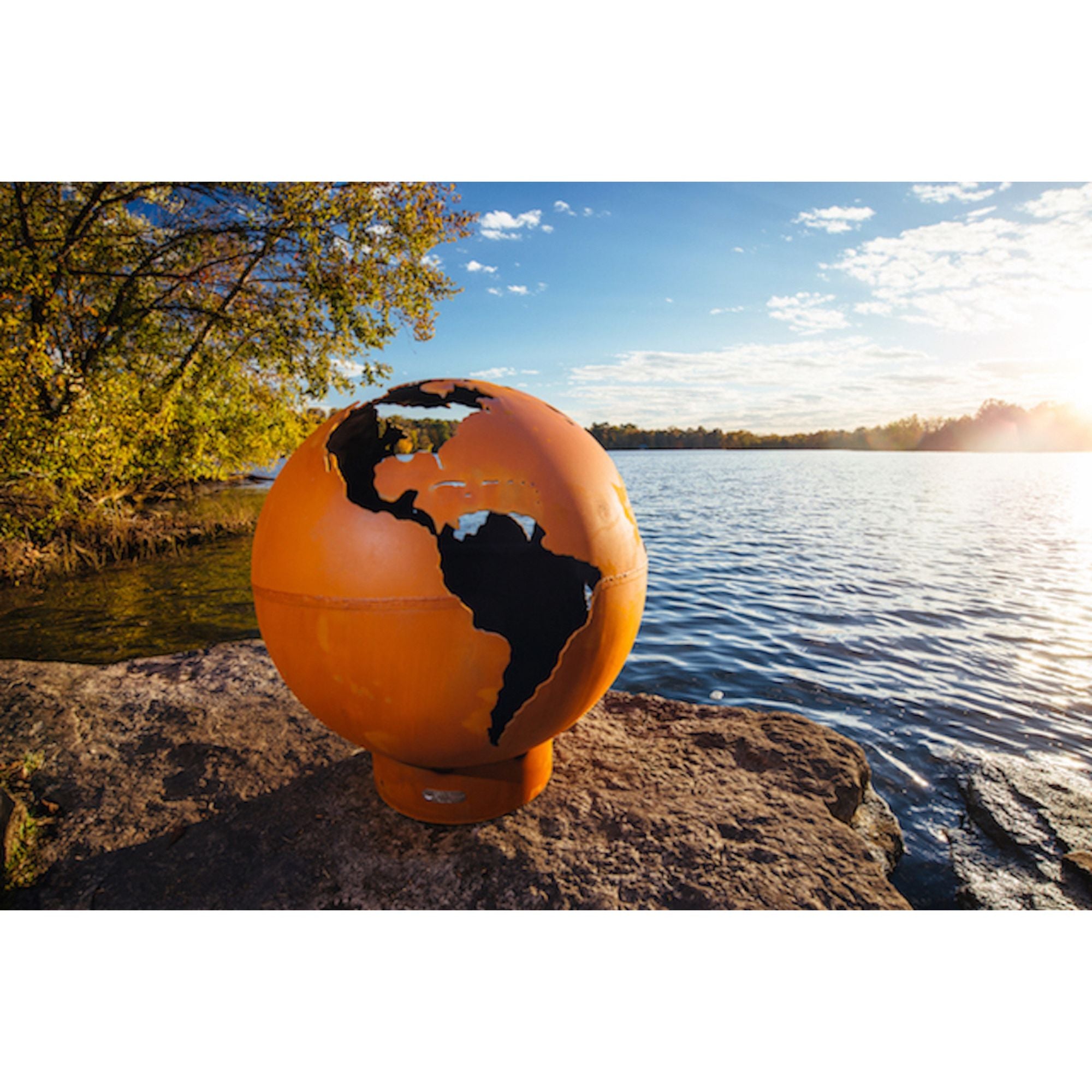 Orange globe with world map design on a rock by a lake